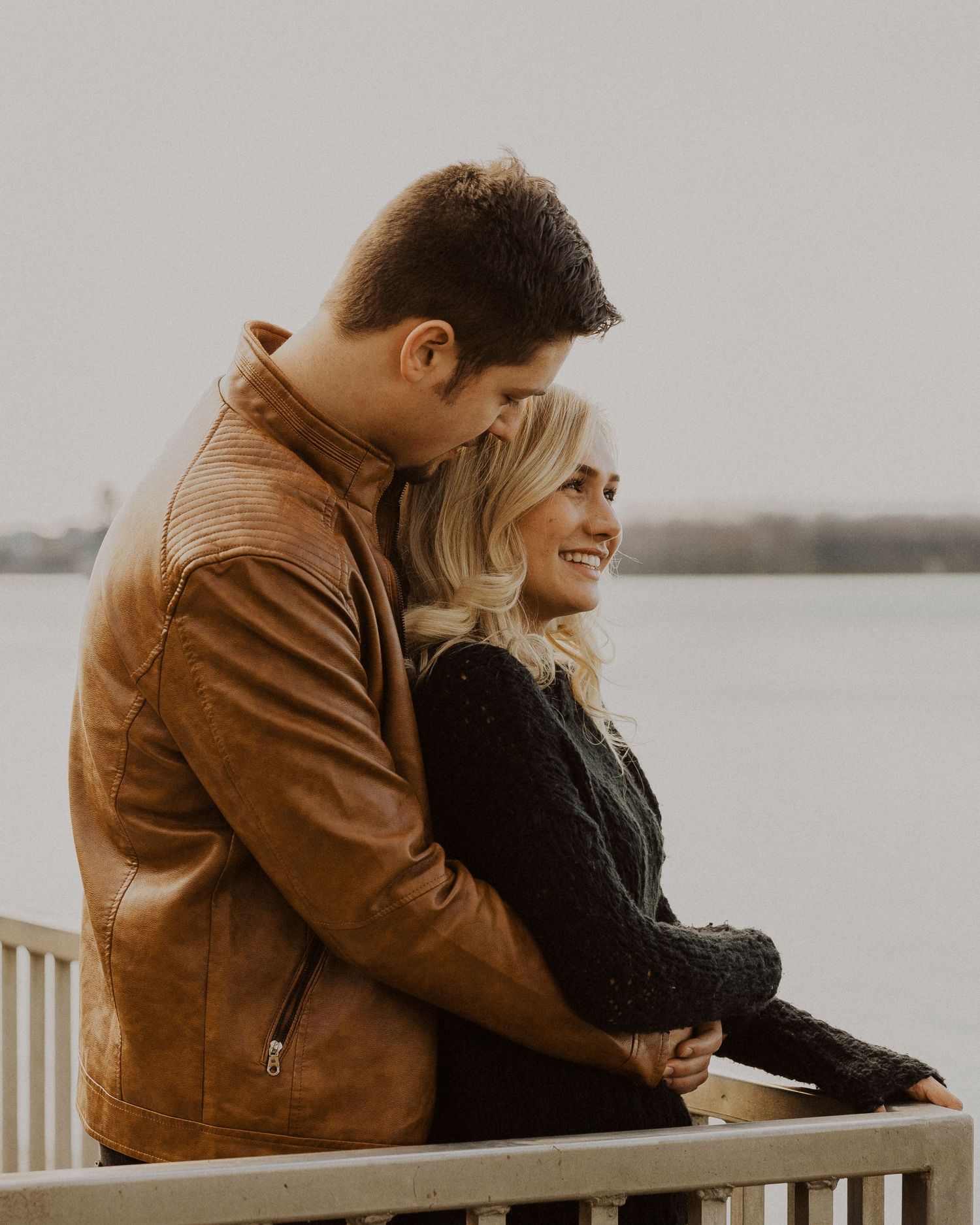 A couple shares intimate moments while sitting on a dock overlooking water.