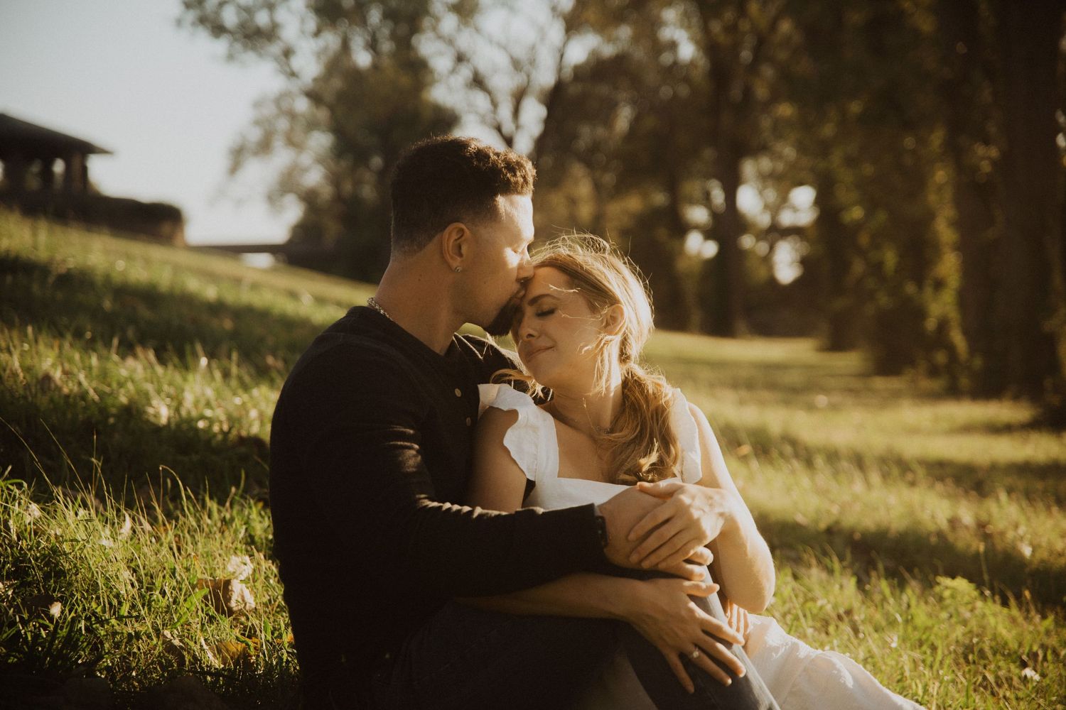Couple shares intimate moment in sunlit field during golden hour photography session.