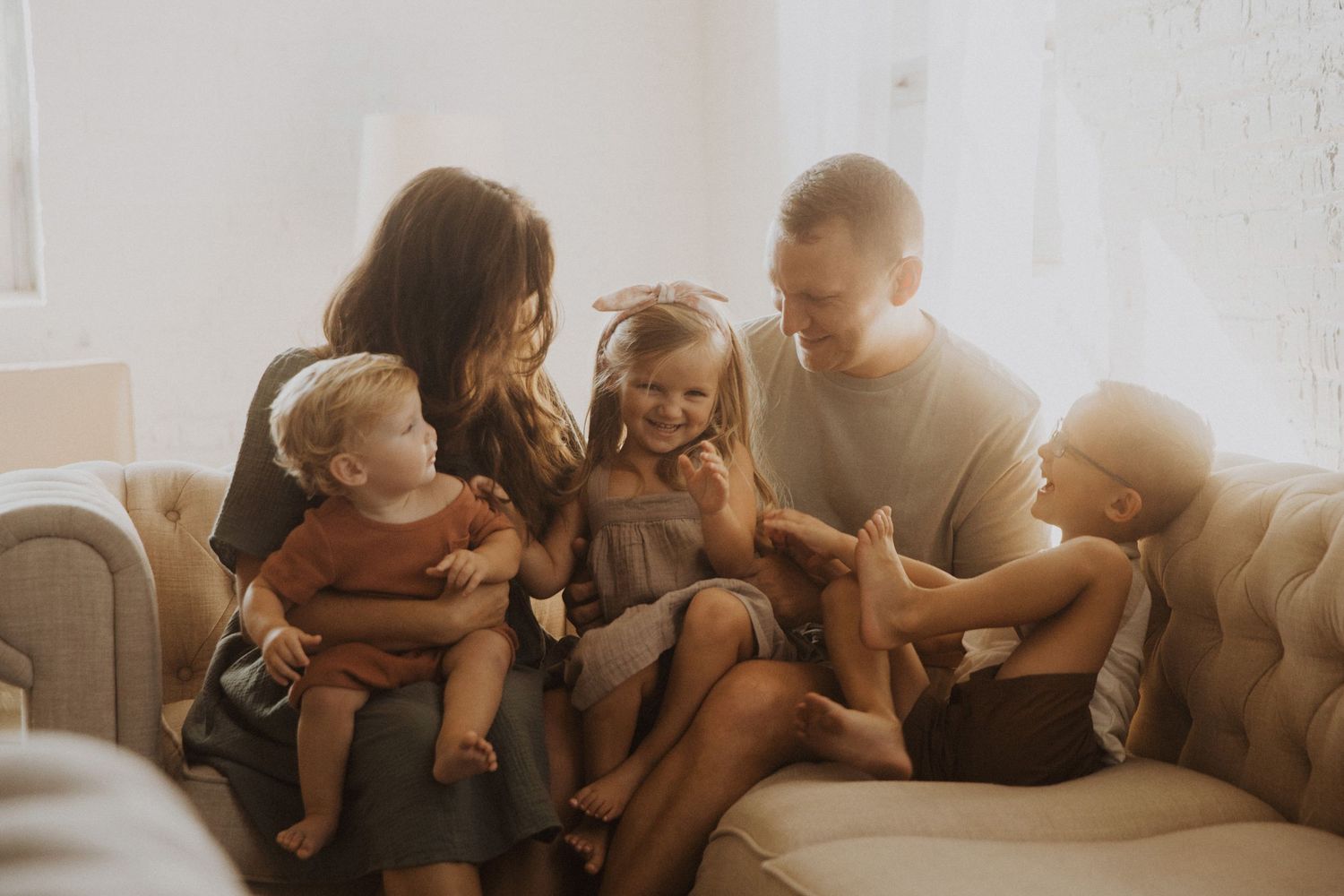 Happy family of five sitting together on a cozy beige sofa, laughing and bonding in a bright, warmly lit living room.