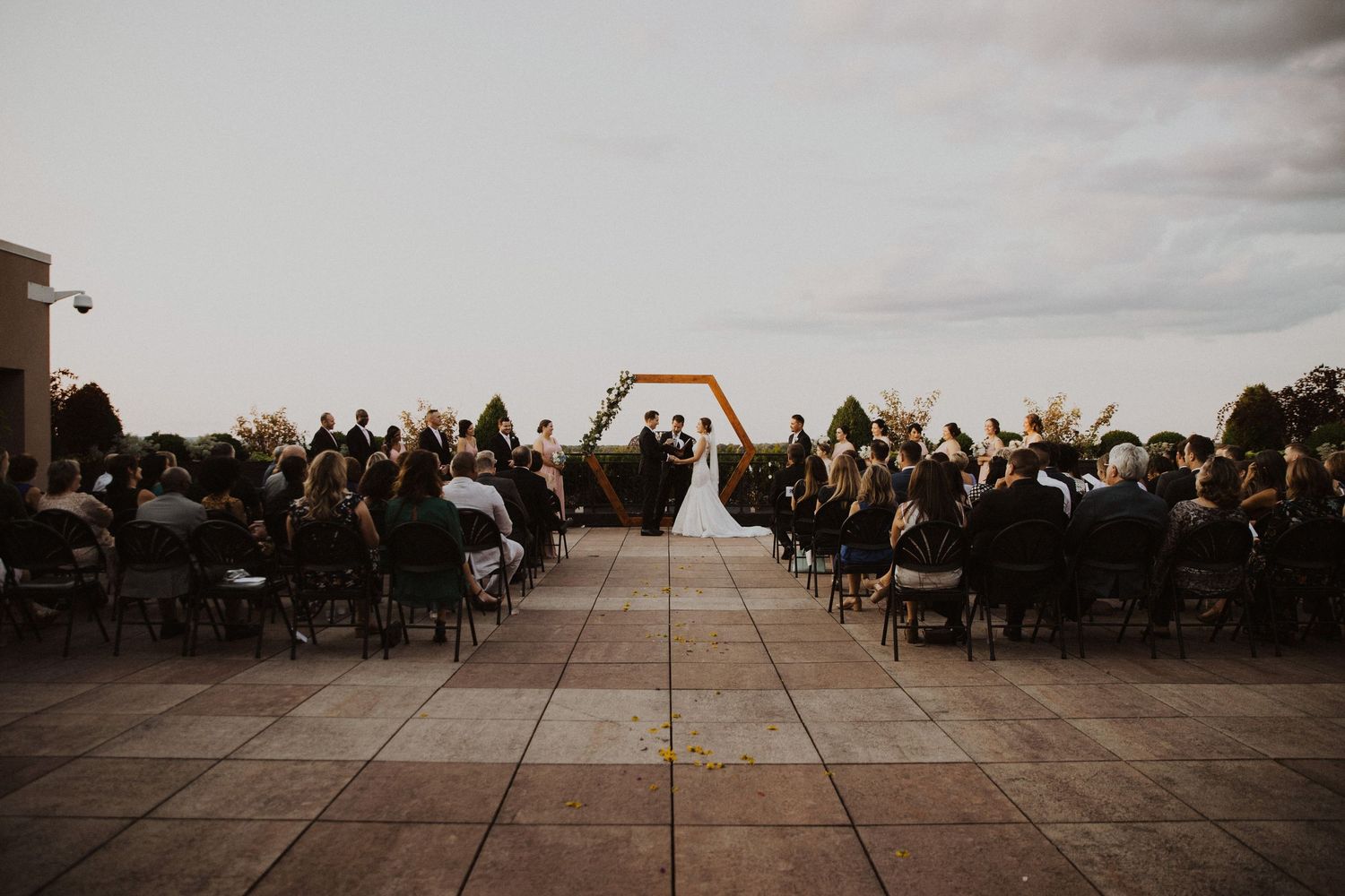 Wide angle view of outdoor wedding ceremony setup with guests seated under cloudy skies.