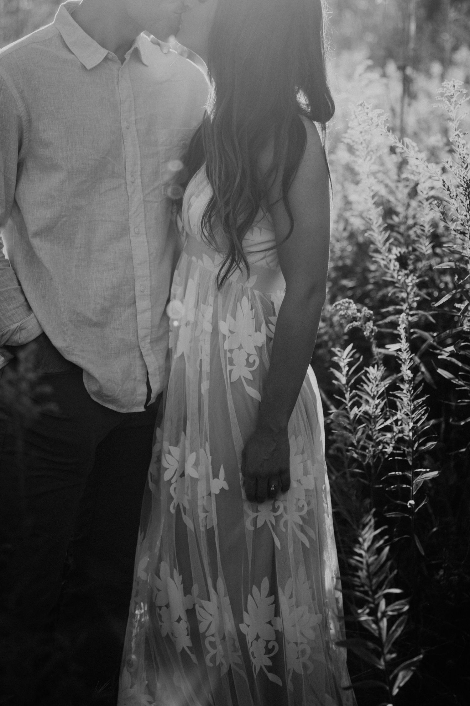 Black and white photo showing couple in formal attire standing in garden setting.