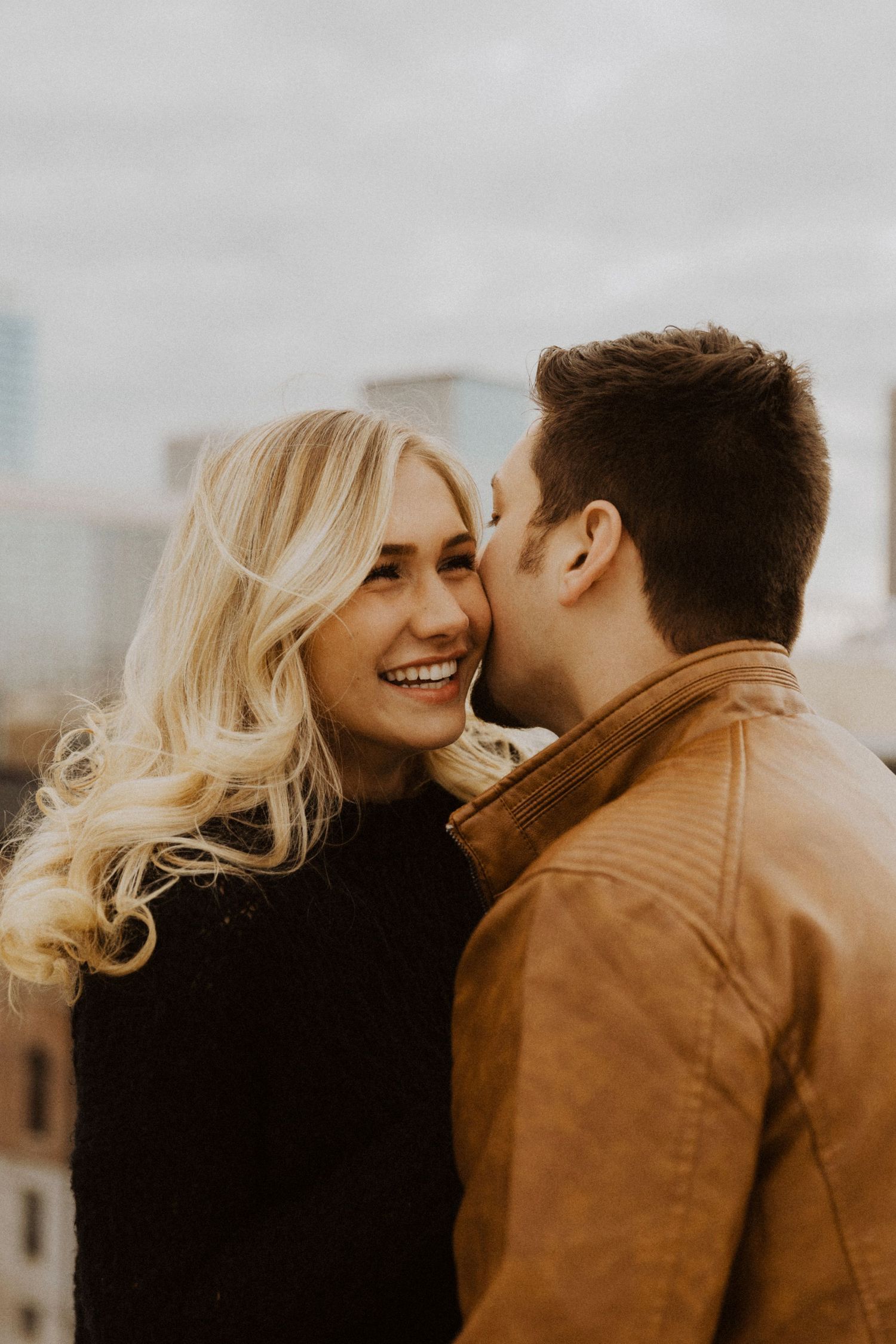 A couple shares an intimate moment against an overcast sky in warm tones.