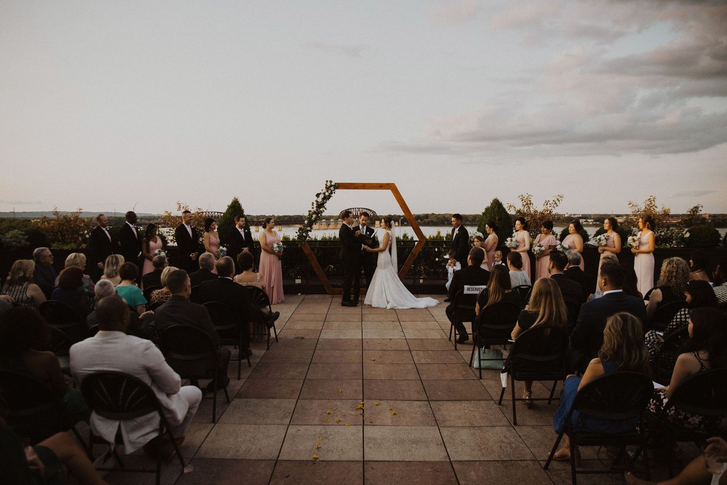 Wide angle view of rooftop wedding ceremony with geometric arch and seated guests.