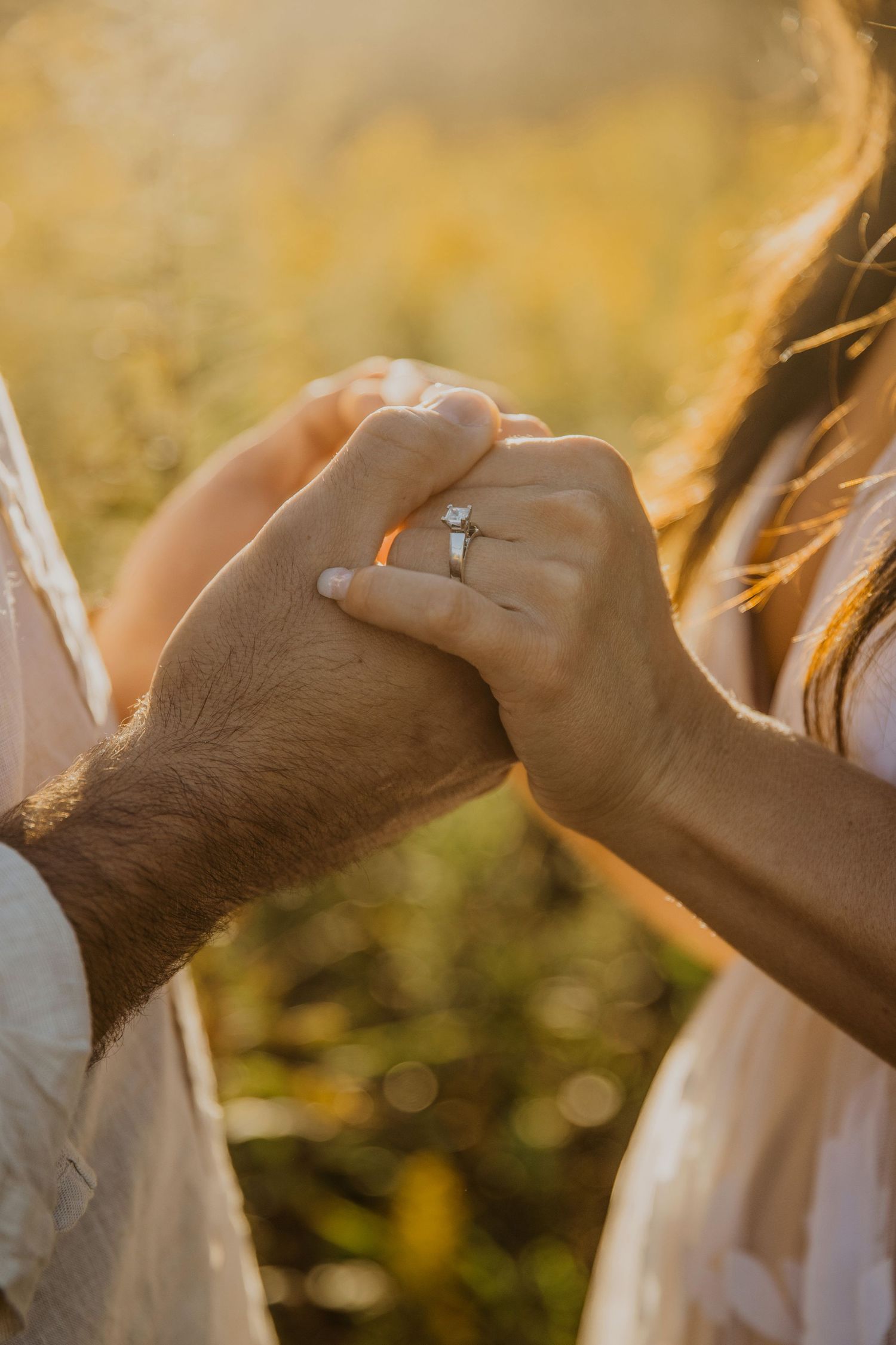 Close-up of hands with engagement ring in golden sunset light.