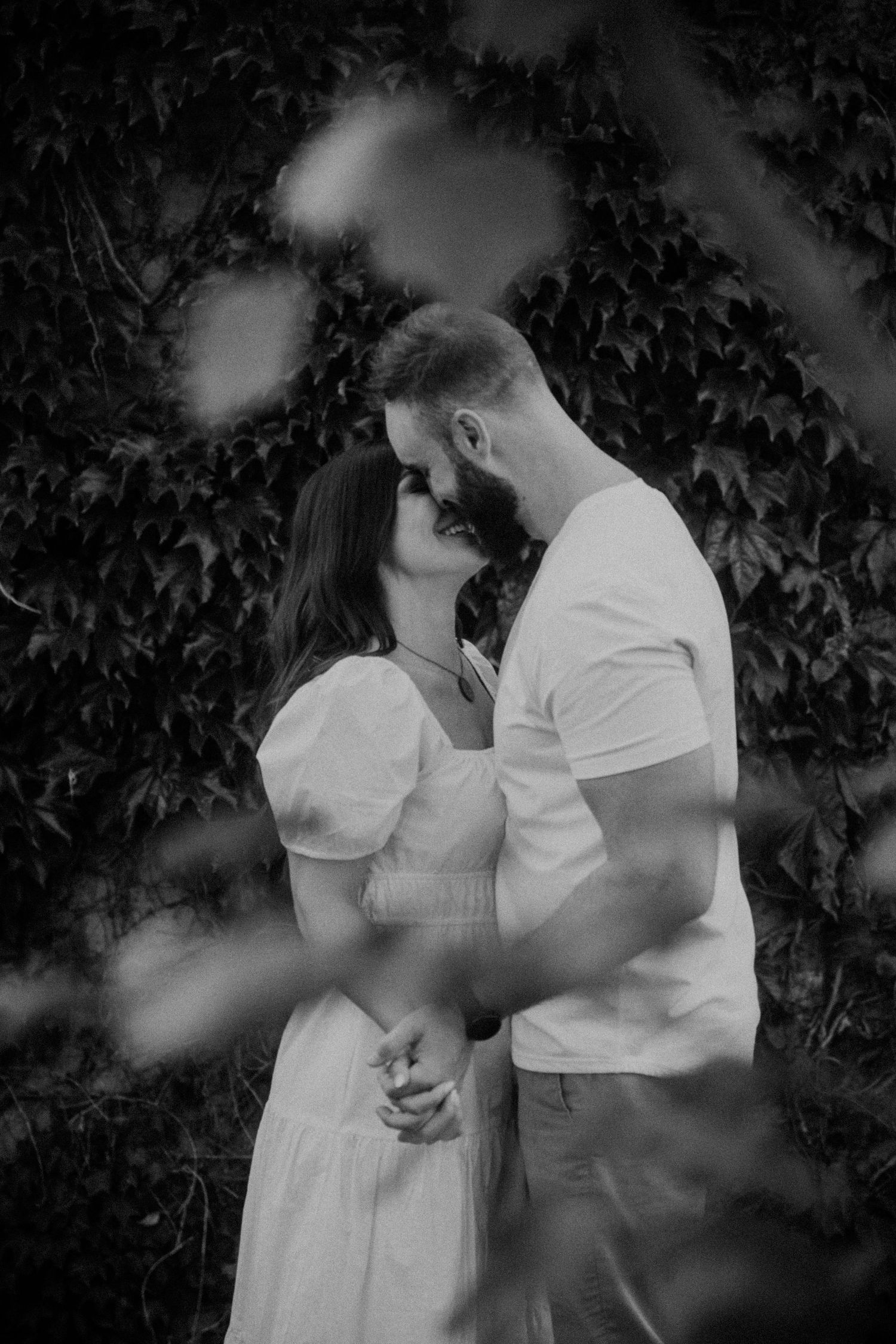 An intimate black and white portrait series of a couple in white clothing against leafy backdrop.