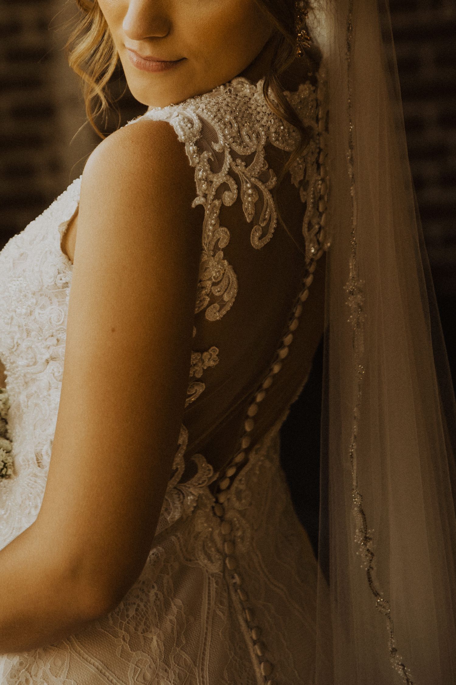 Wedding dress detail shot highlighting intricate lace pattern and buttons in warm tones.