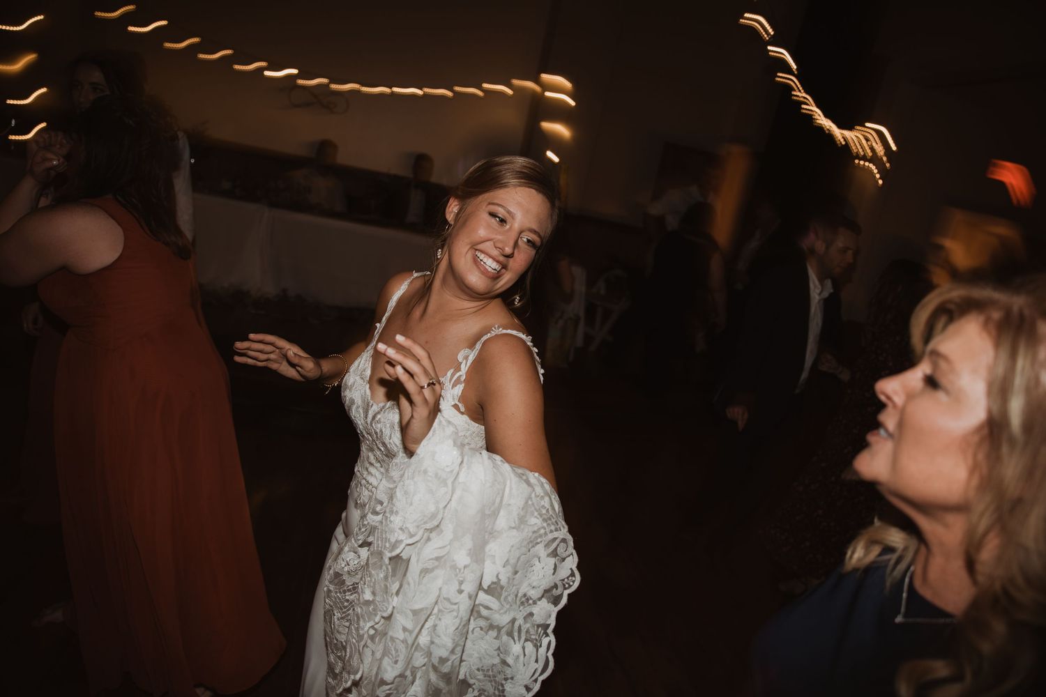 Celebration on the dance floor with bride in white lace dress at wedding reception.