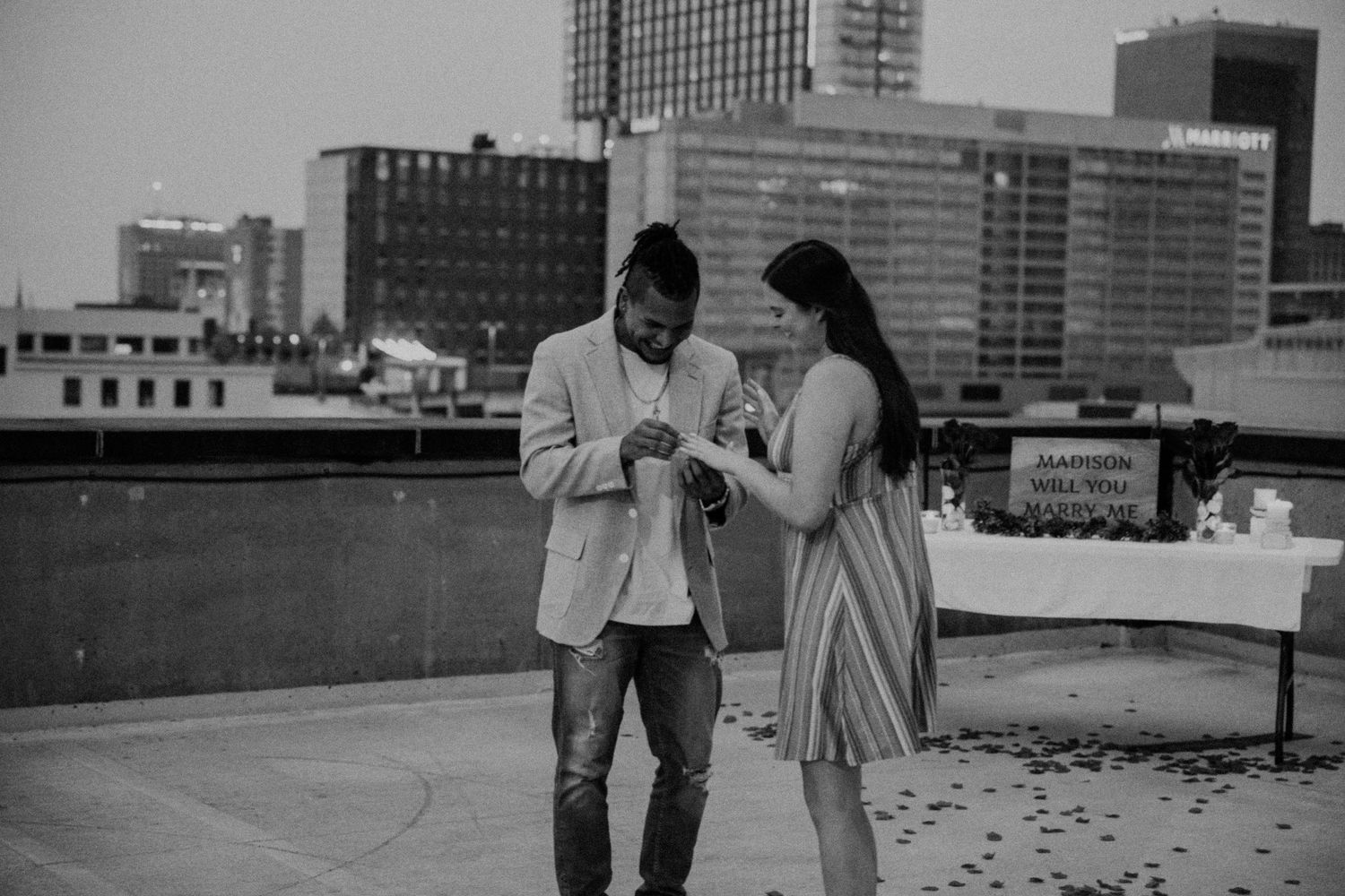 Black and white photo of a romantic rooftop scene with city buildings in background.