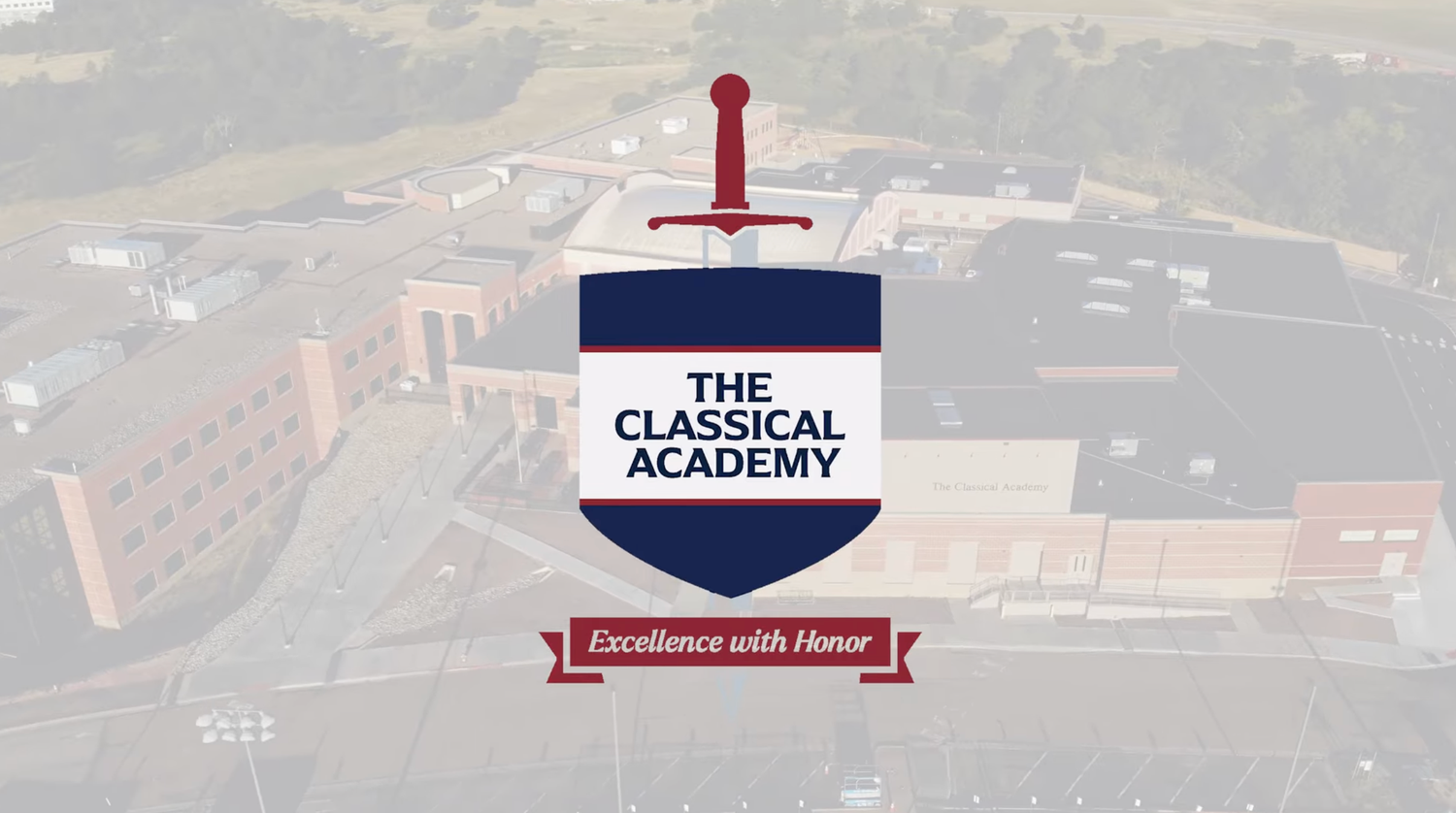 Aerial view of a red-roofed classical academy building complex with signage and surrounding landscape.