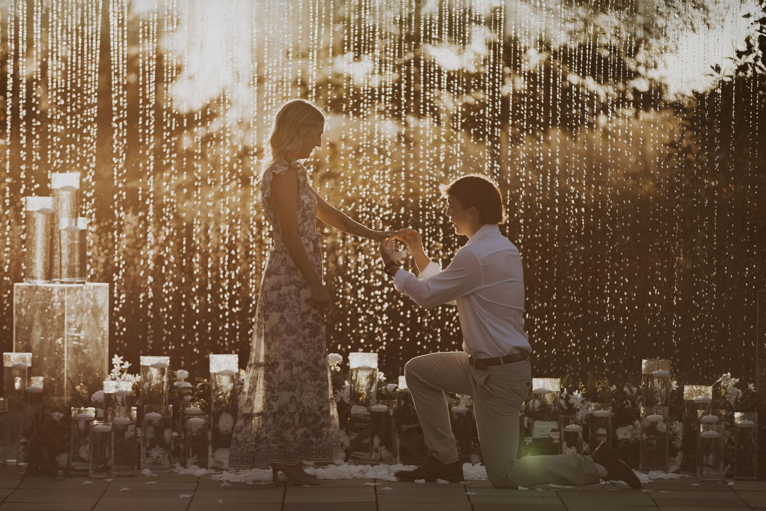 Marriage proposal moment captured at sunset with string lights and candles creating magical atmosphere.