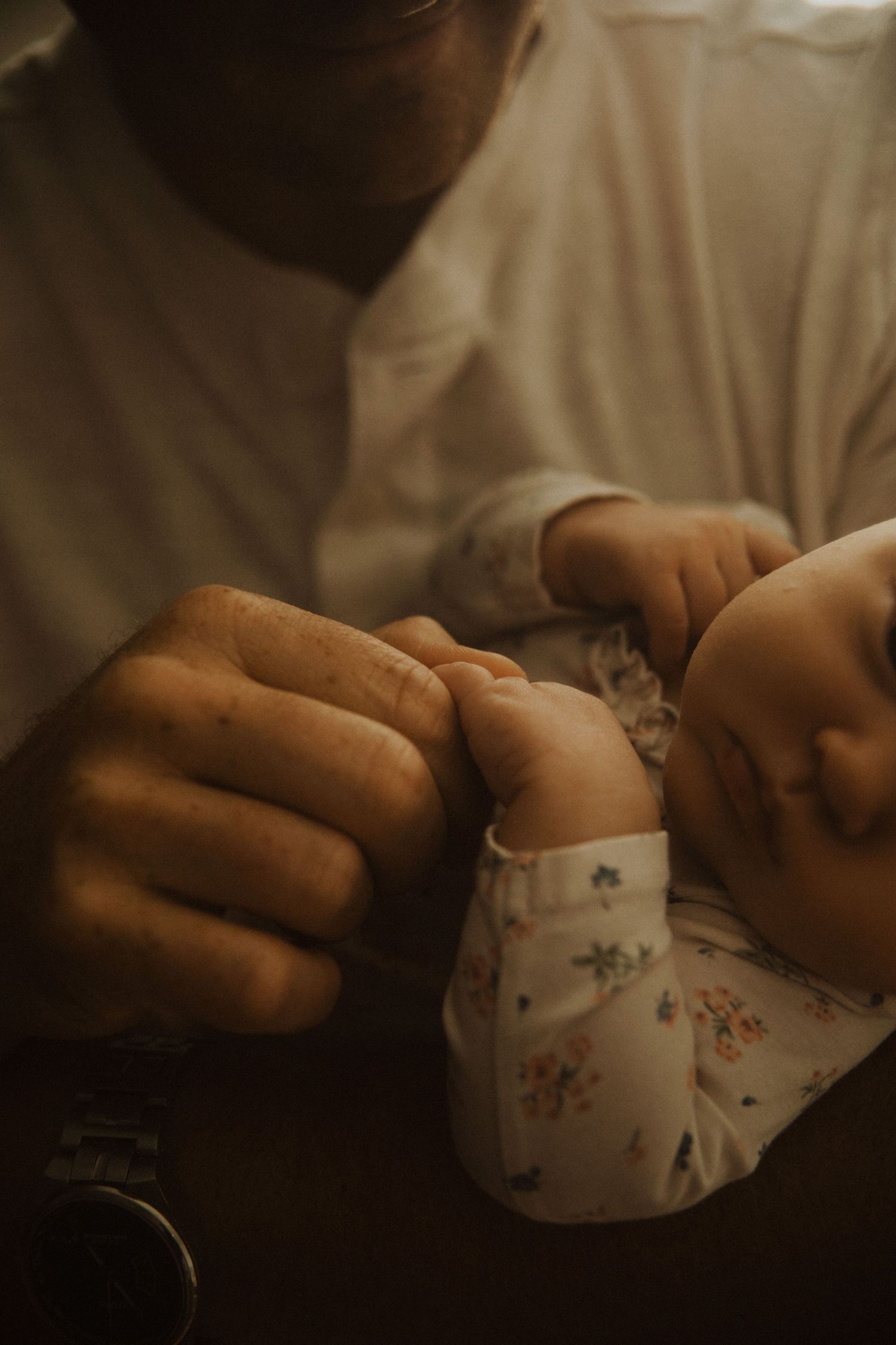 A parent gently holds a sleeping newborn baby dressed in a floral onesie, capturing a tender bonding moment.