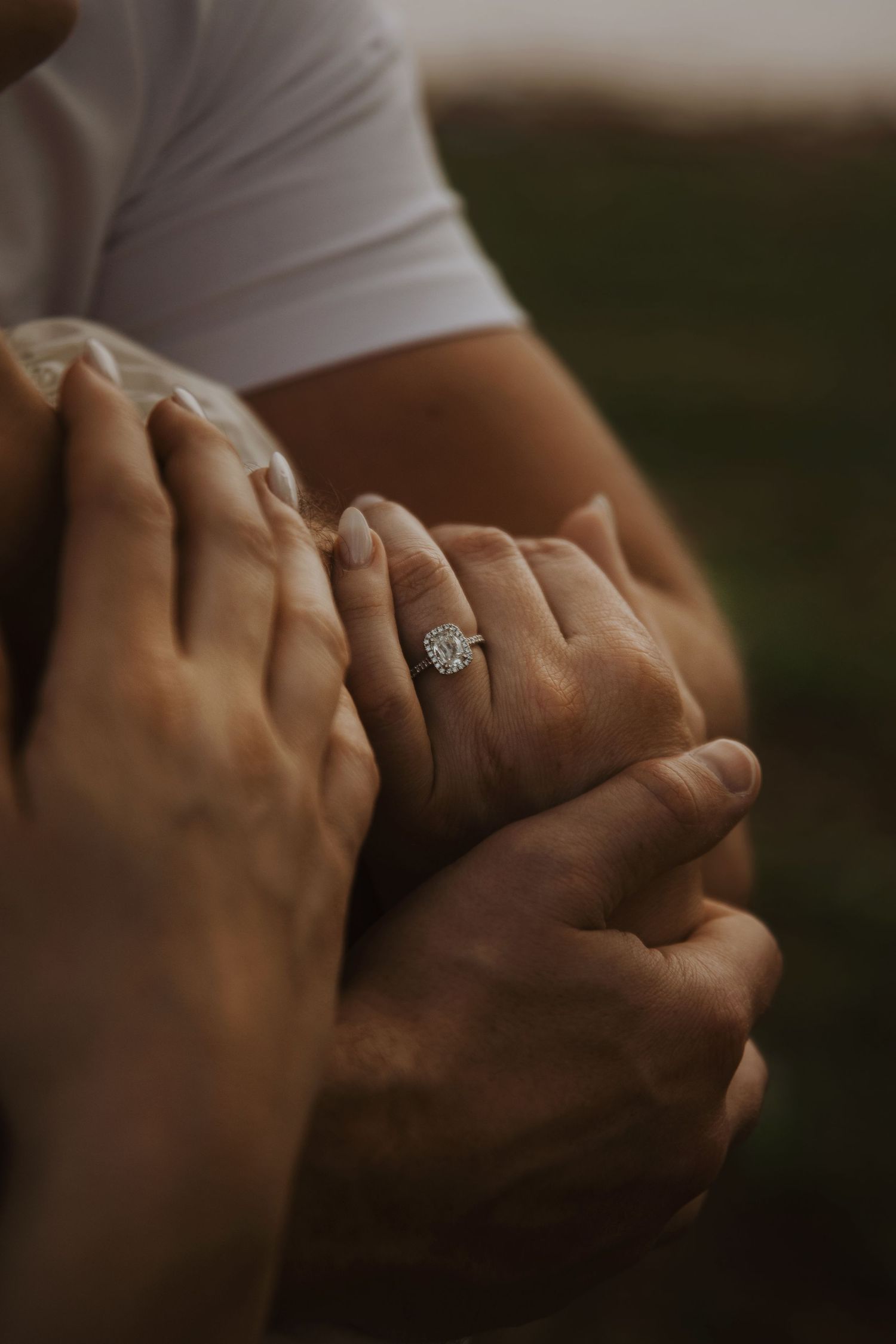 Close-up of intertwined hands with engagement ring in warm lighting.