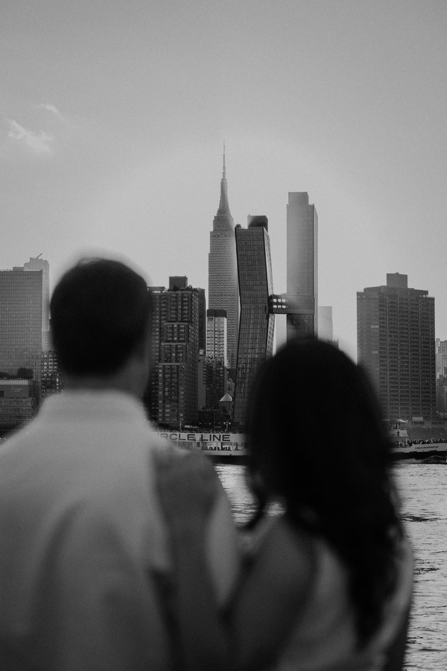 Black and white photo of a couple gazing at the New York City skyline across the river.