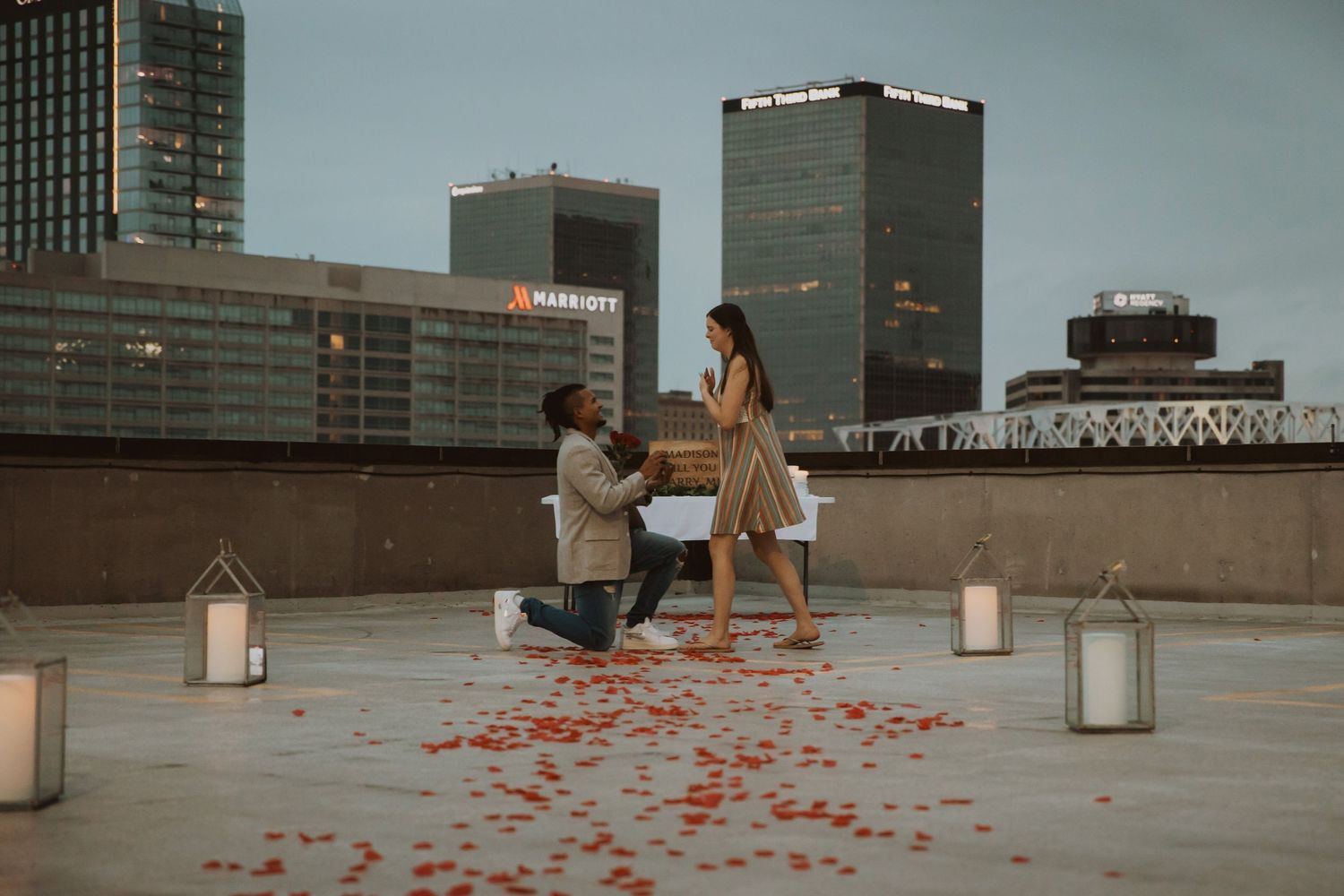 A rooftop setting with lanterns and rose petals scattered across the ground at dusk.