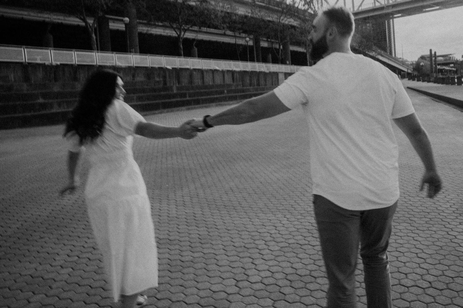 A couple walks hand in hand on brick pavement in black and white photography.