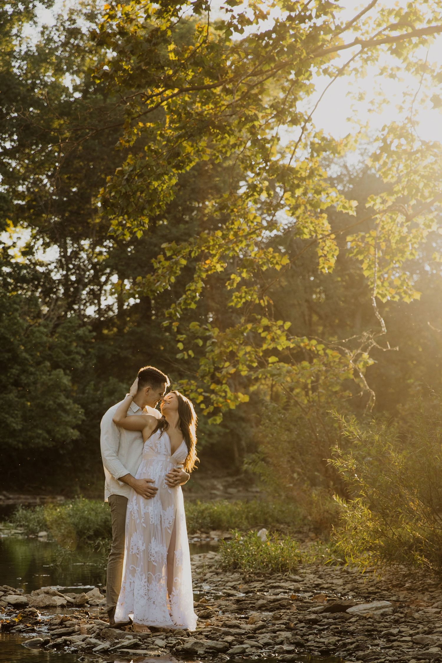 A romantic couple in white outfits share an intimate moment at sunset in a garden setting.