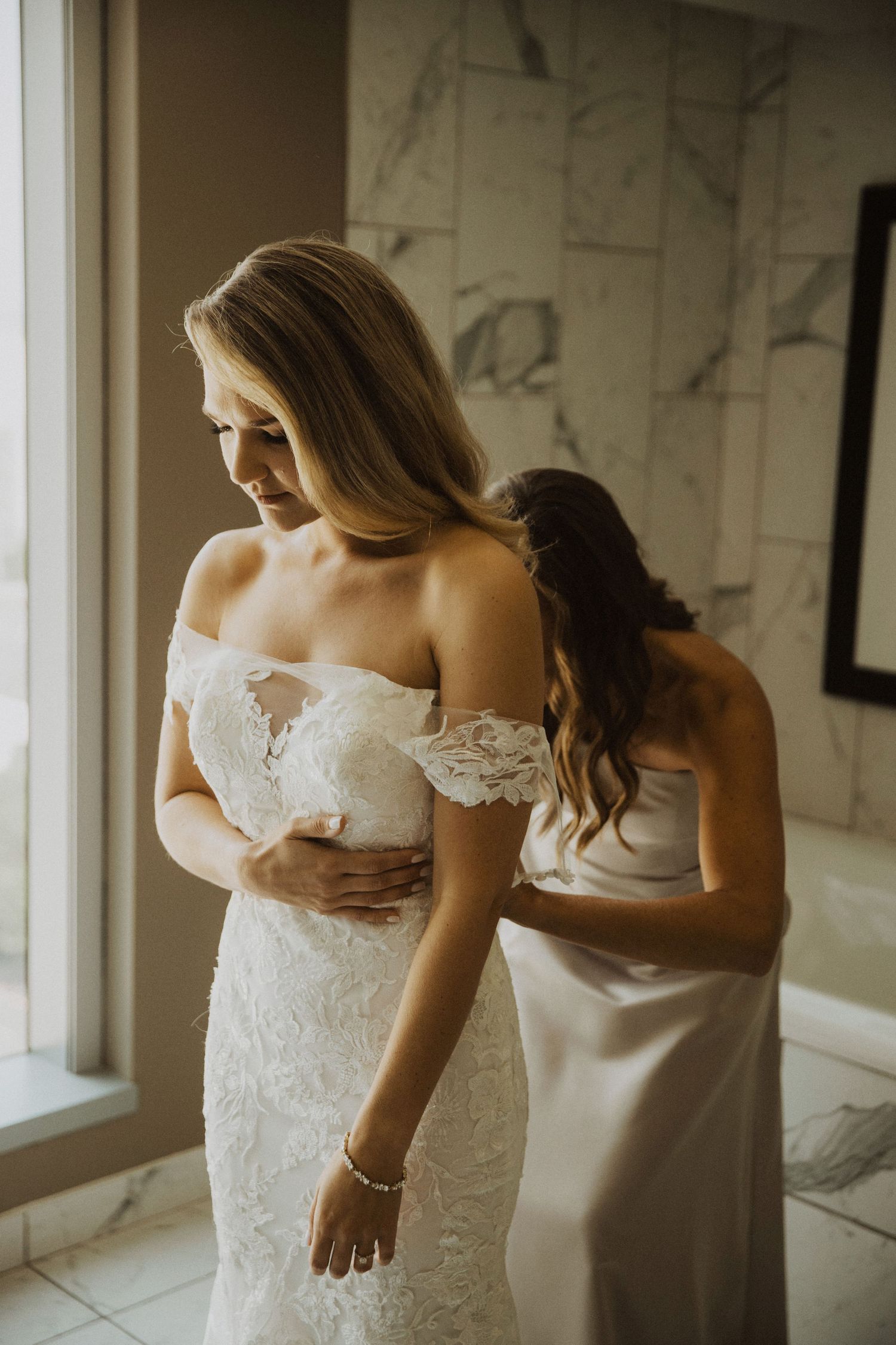 Behind the scenes of bride getting dressed with help from wedding party.