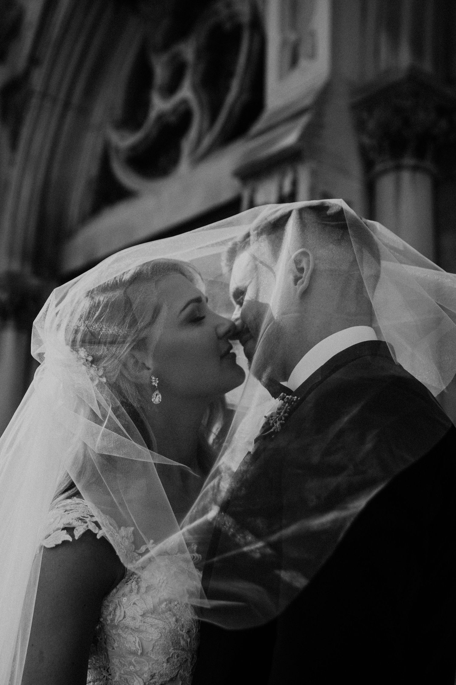 Romantic black and white portrait of newlyweds sharing their first kiss through bridal veil.