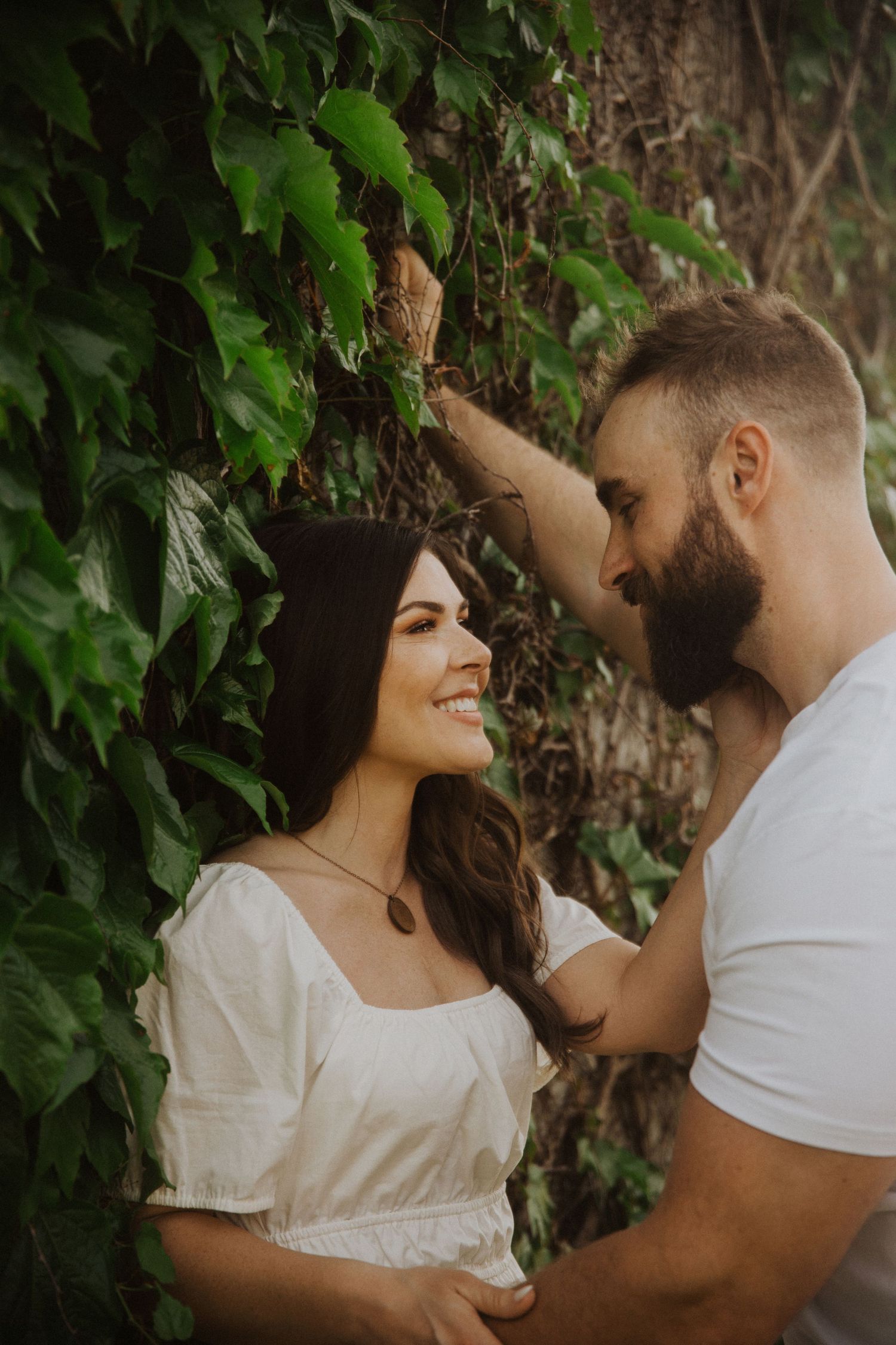 Couple in white clothing sharing intimate moments against a backdrop of green ivy.