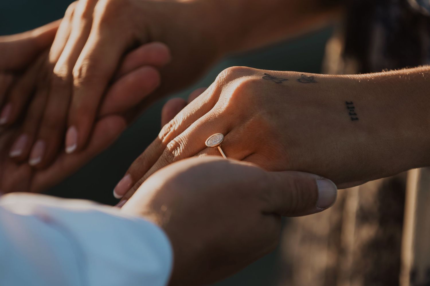 Close-up of hands exchanging engagement ring in soft natural lighting.