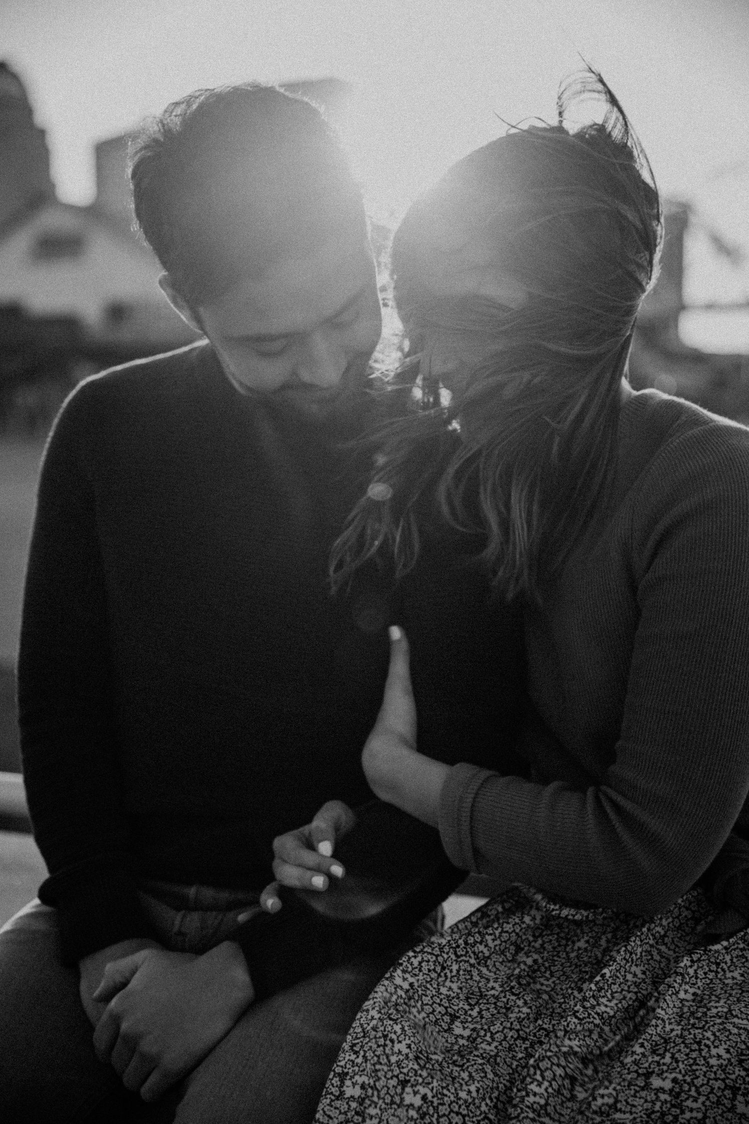 Black and white photo of couple sharing intimate moment in backlit setting.