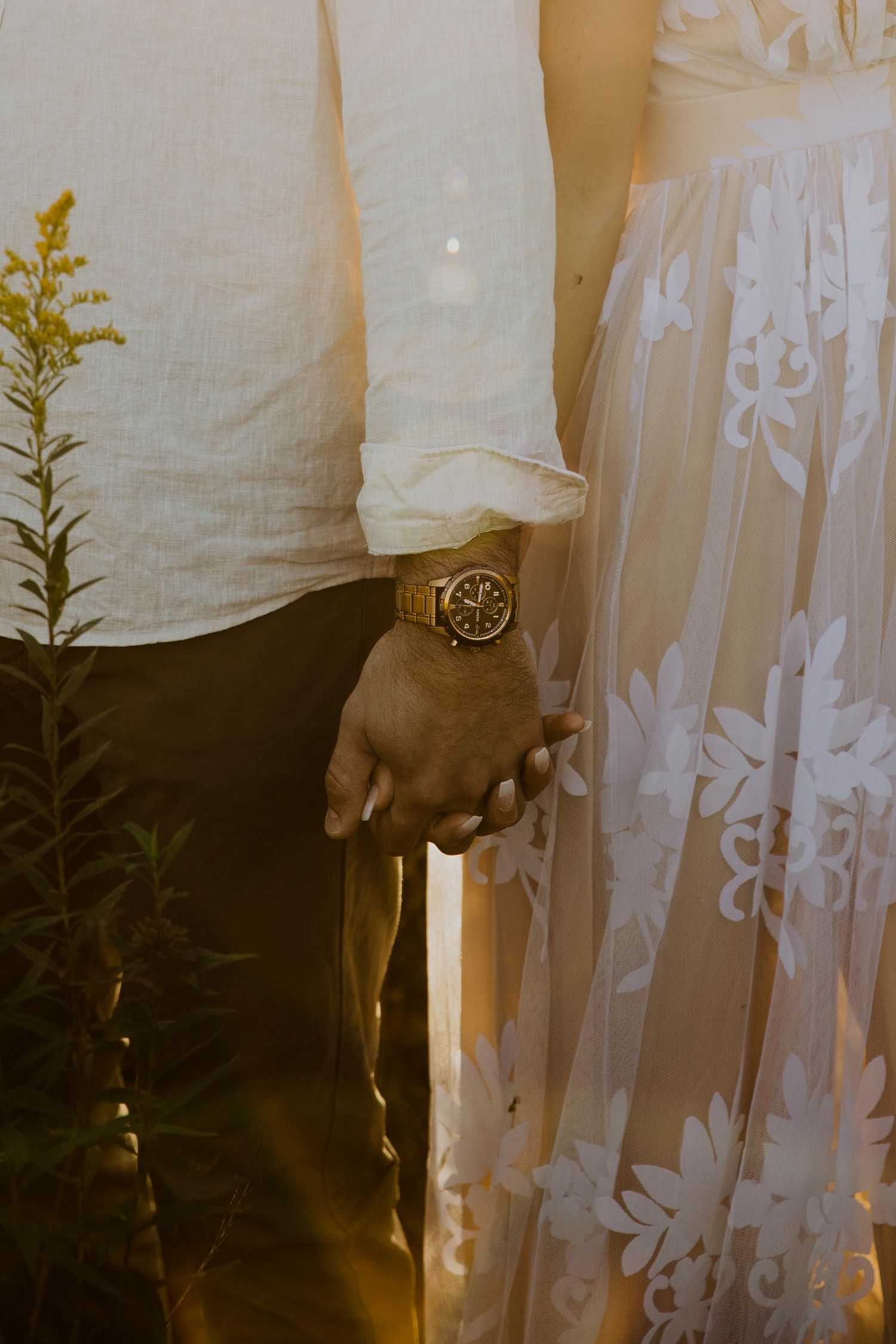 A couple embraces in white clothing against a delicate lace curtain background.