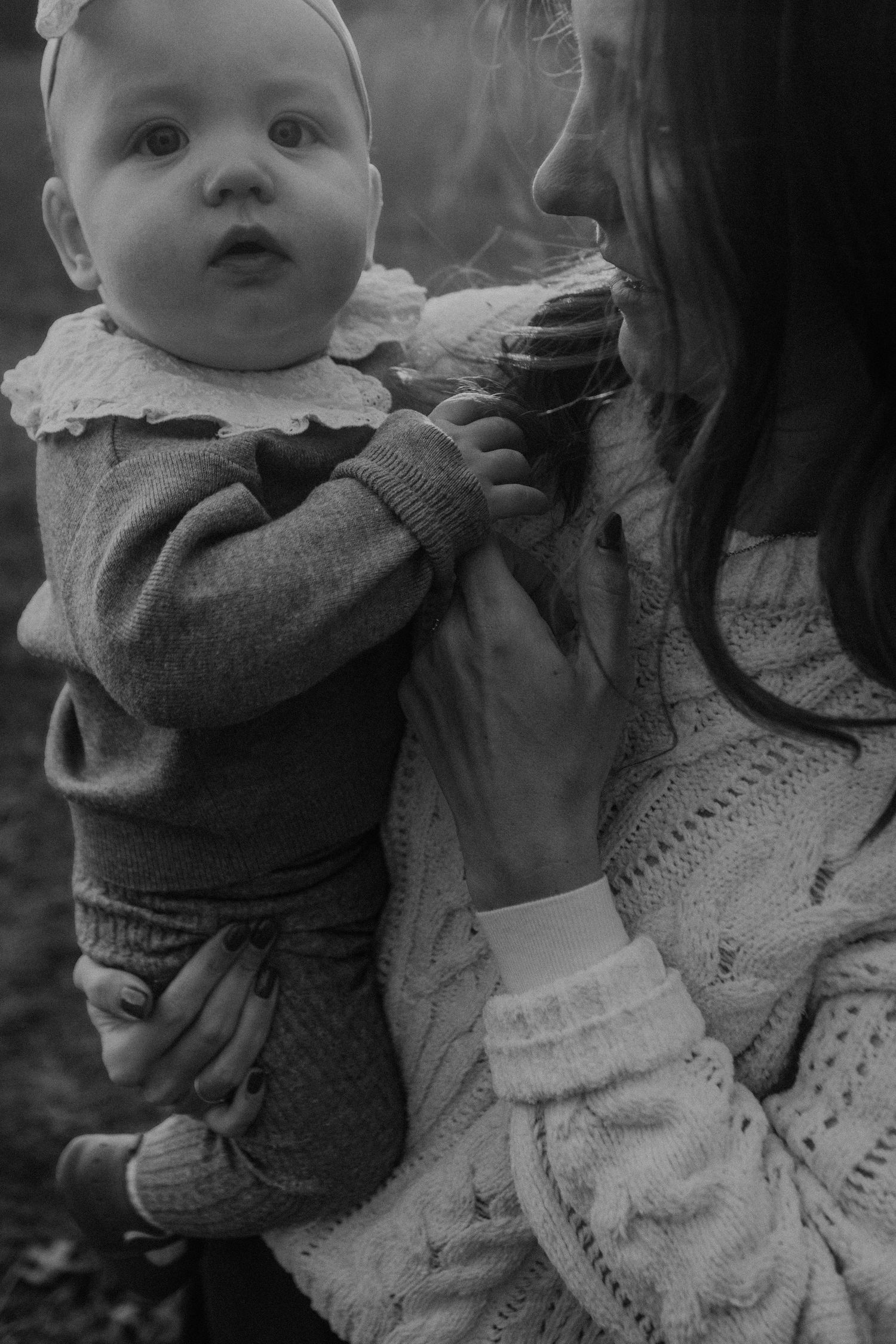 Black and white photo of a mother holding her baby in a knit sweater outdoors.