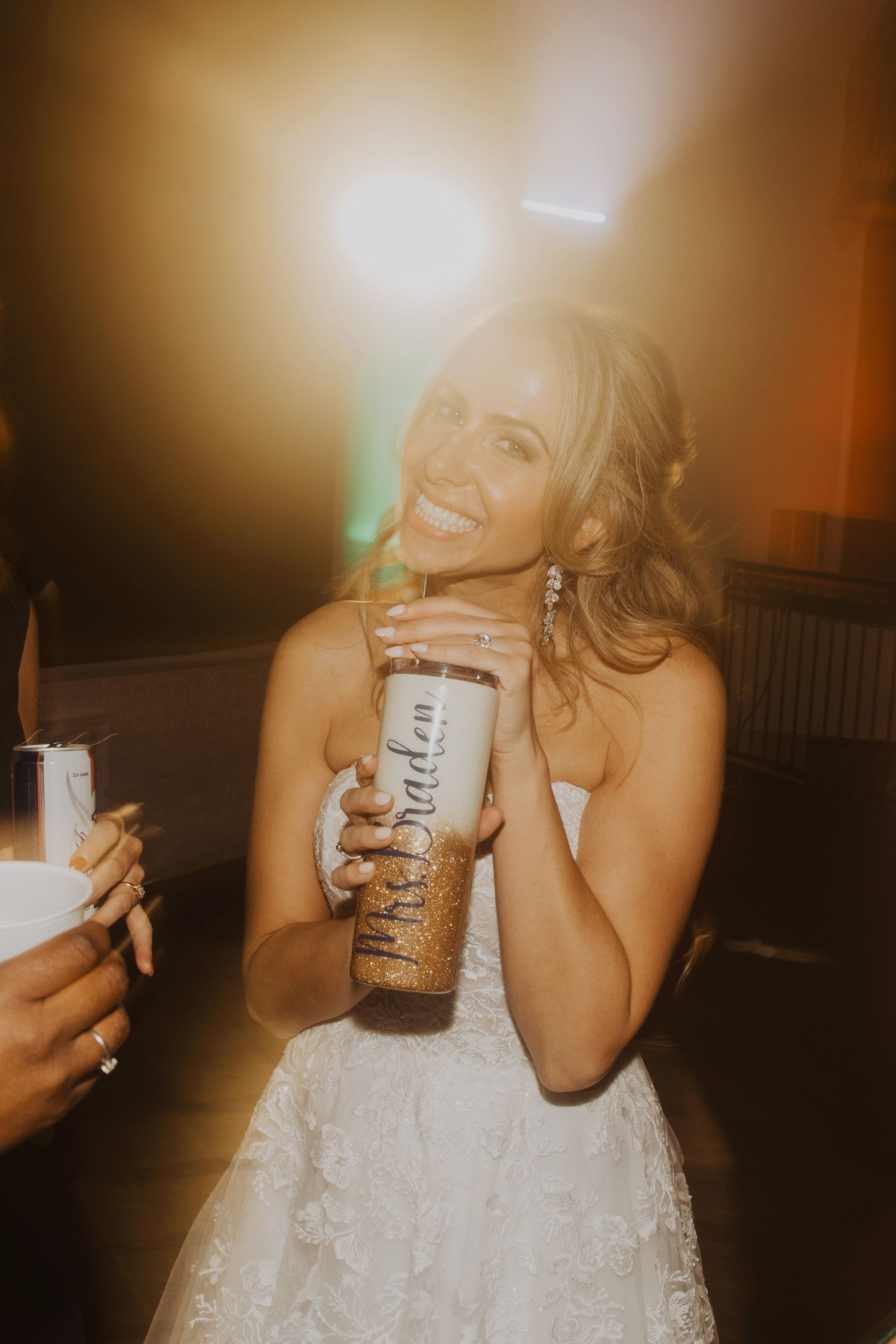 Bride in white lace dress enjoying a drink during wedding reception celebrations.