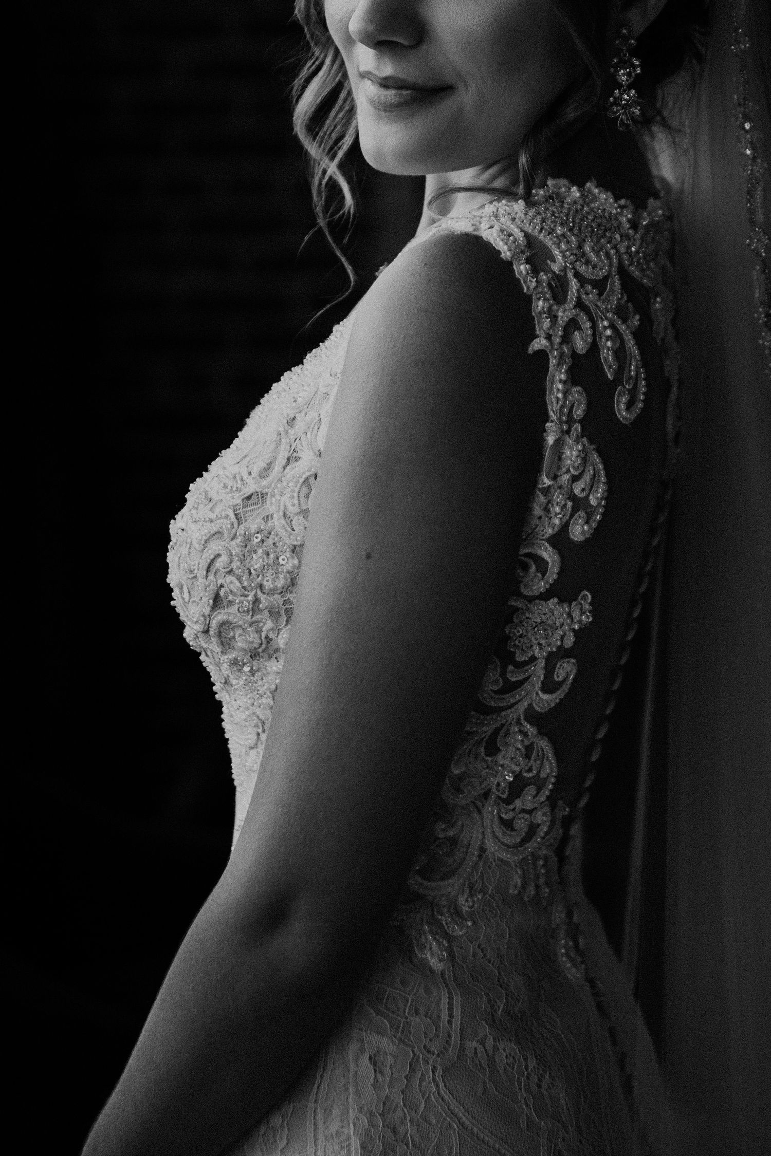 Side profile of wedding dress showing ornate lace detailing against dark background.