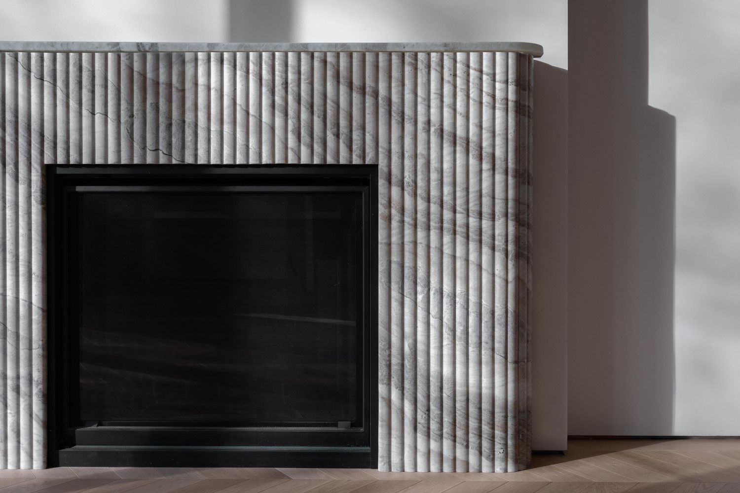 Minimalist fluted marble fireplace surround with black insert in contemporary living space.