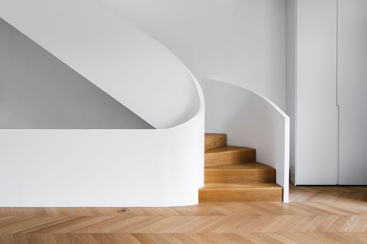 Elegant curved white staircase with warm oak wood steps and herringbone parquet flooring.