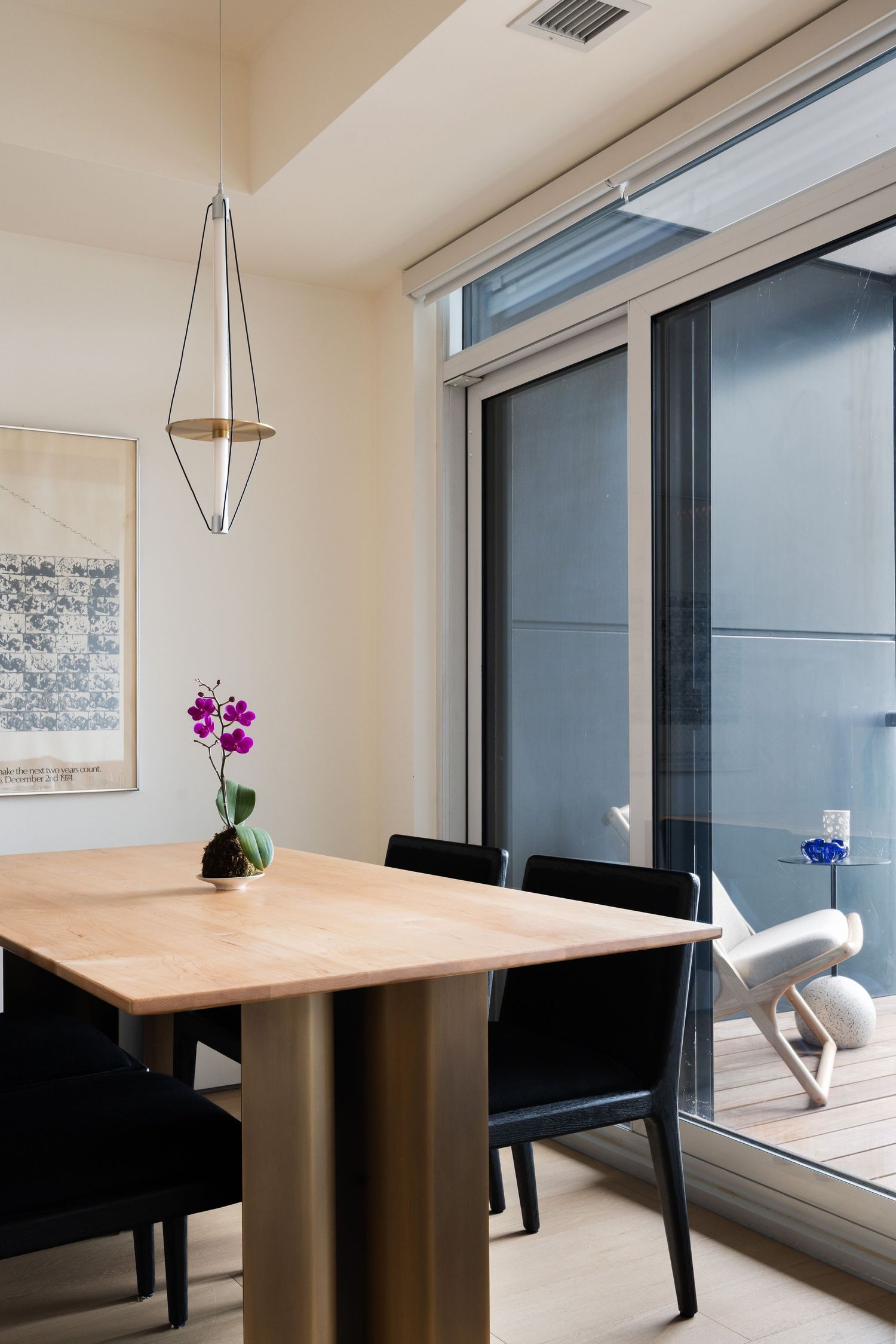 Dining area with wooden table, black chairs, orchid, geometric pendant, and sliding doors to balcony.