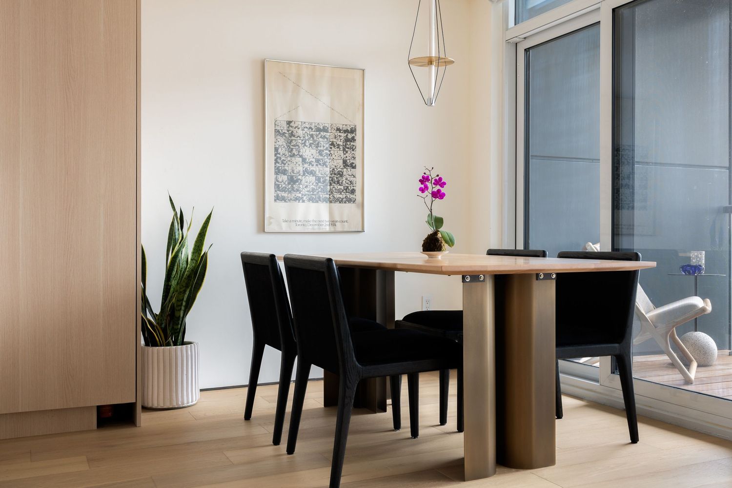 Contemporary dining area with wooden table, black chairs, orchid centerpiece, and geometric pendant light.