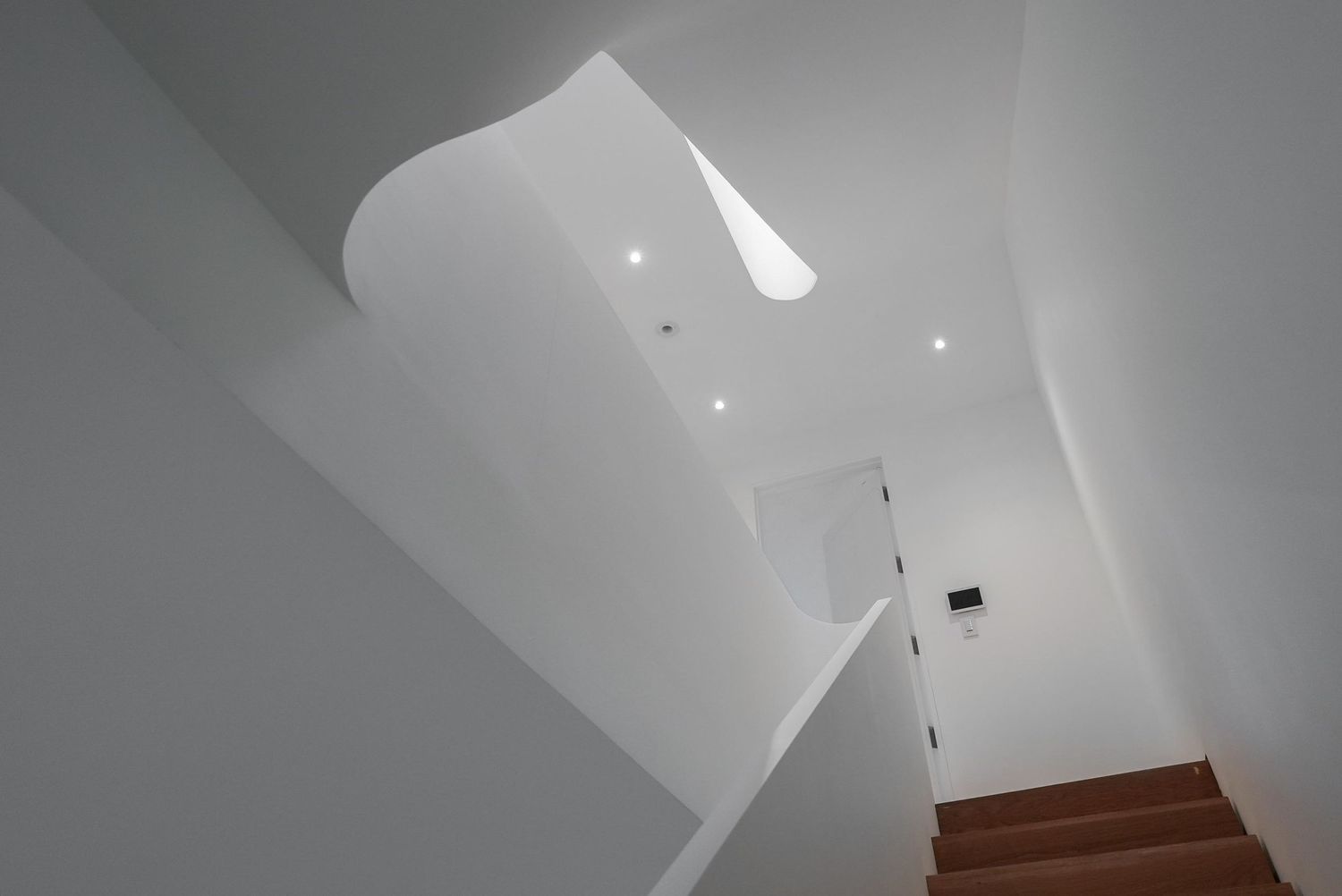 Dramatic white sculptural stairwell ceiling with recessed lighting and angular geometric design.