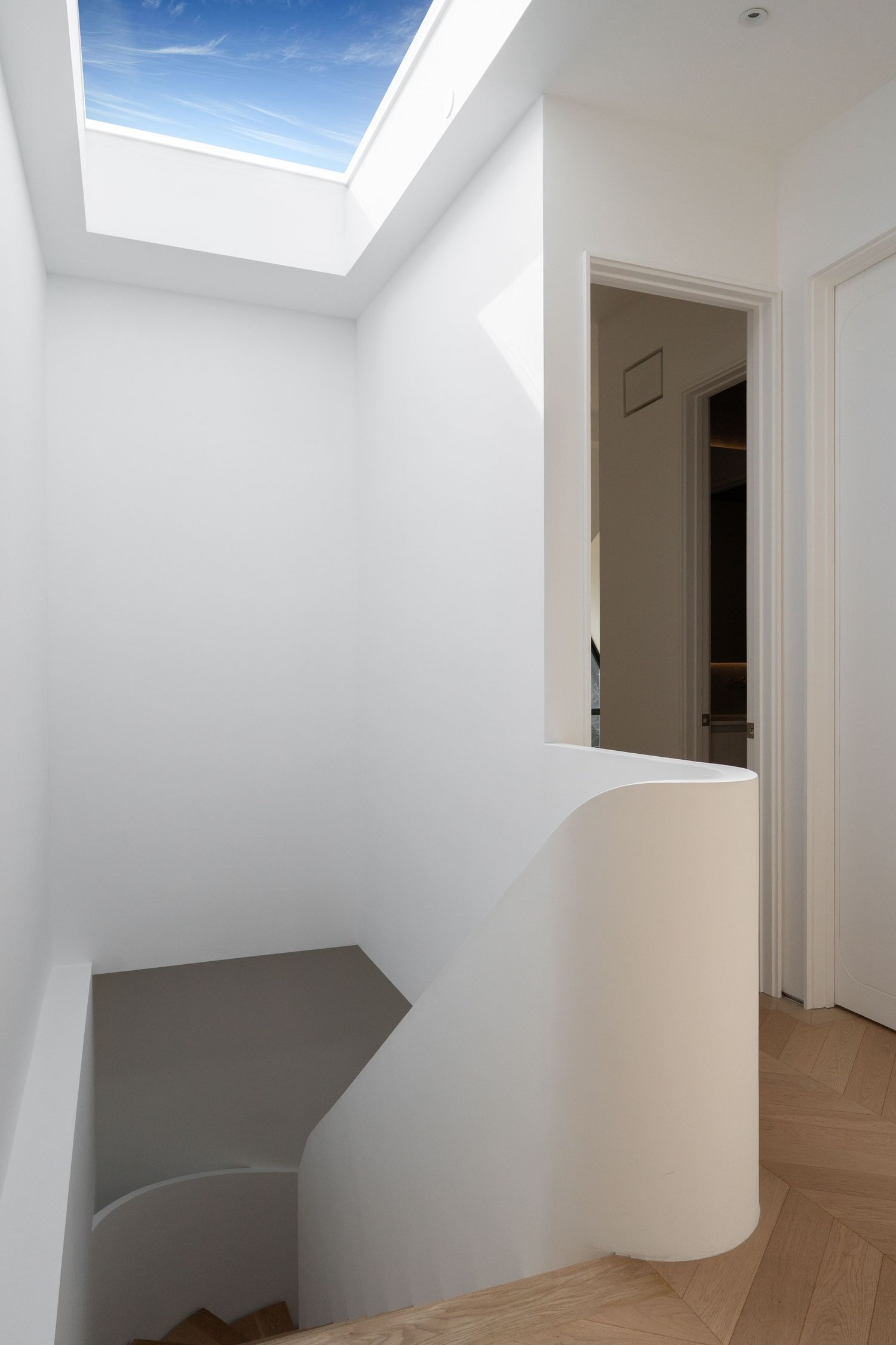 Modern white stairwell with skylight offering natural light and herringbone wood floors.