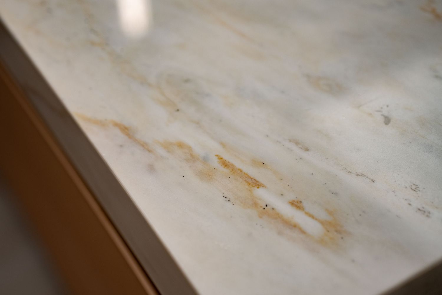 Close-up of white marble countertop with golden veining on warm wood cabinet edge.