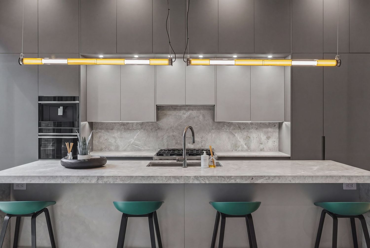 Modern gray kitchen with marble island, teal bar stools, gold pendant light, and stainless steel appliances.