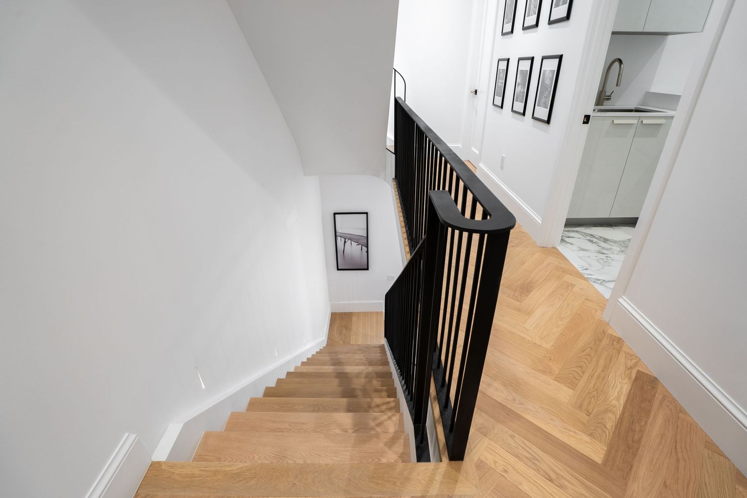 Modern staircase with herringbone hardwood floors, black spindle railing, and white walls in a stylish home interior.