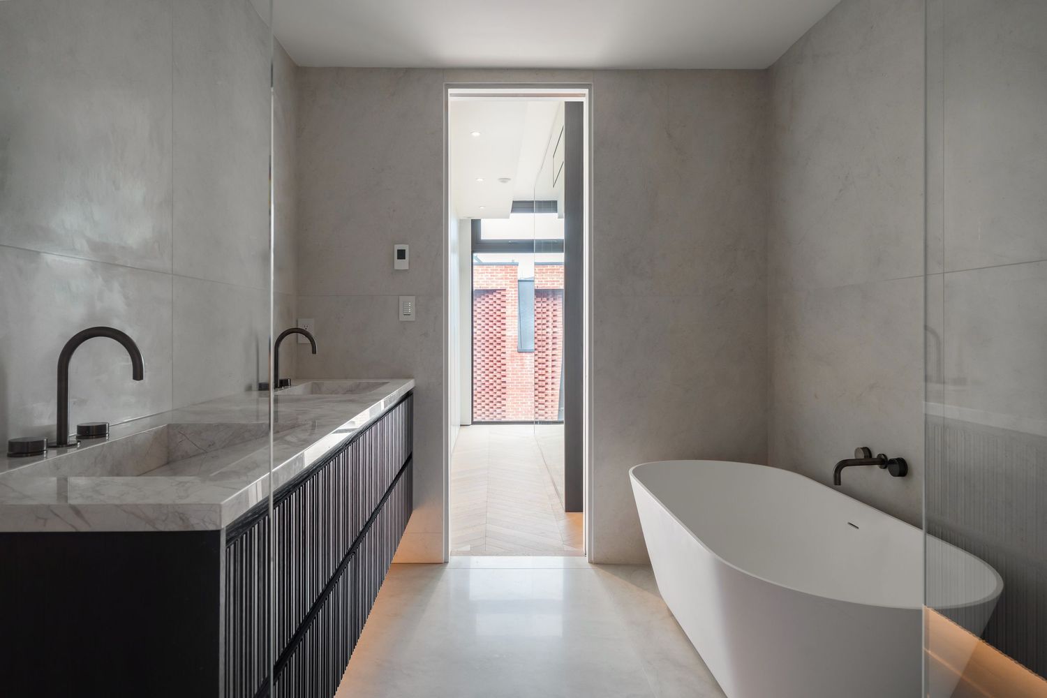 Modern minimalist bathroom with concrete walls, freestanding white tub, black vanity, and natural light from tall window.