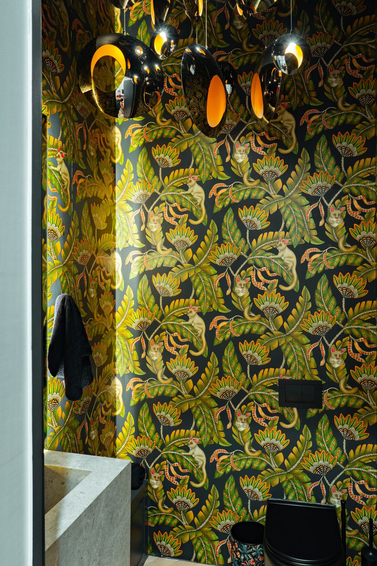 Bold tropical floral wallpaper in green and gold tones adorns a stylish bathroom with modern pendant lights.