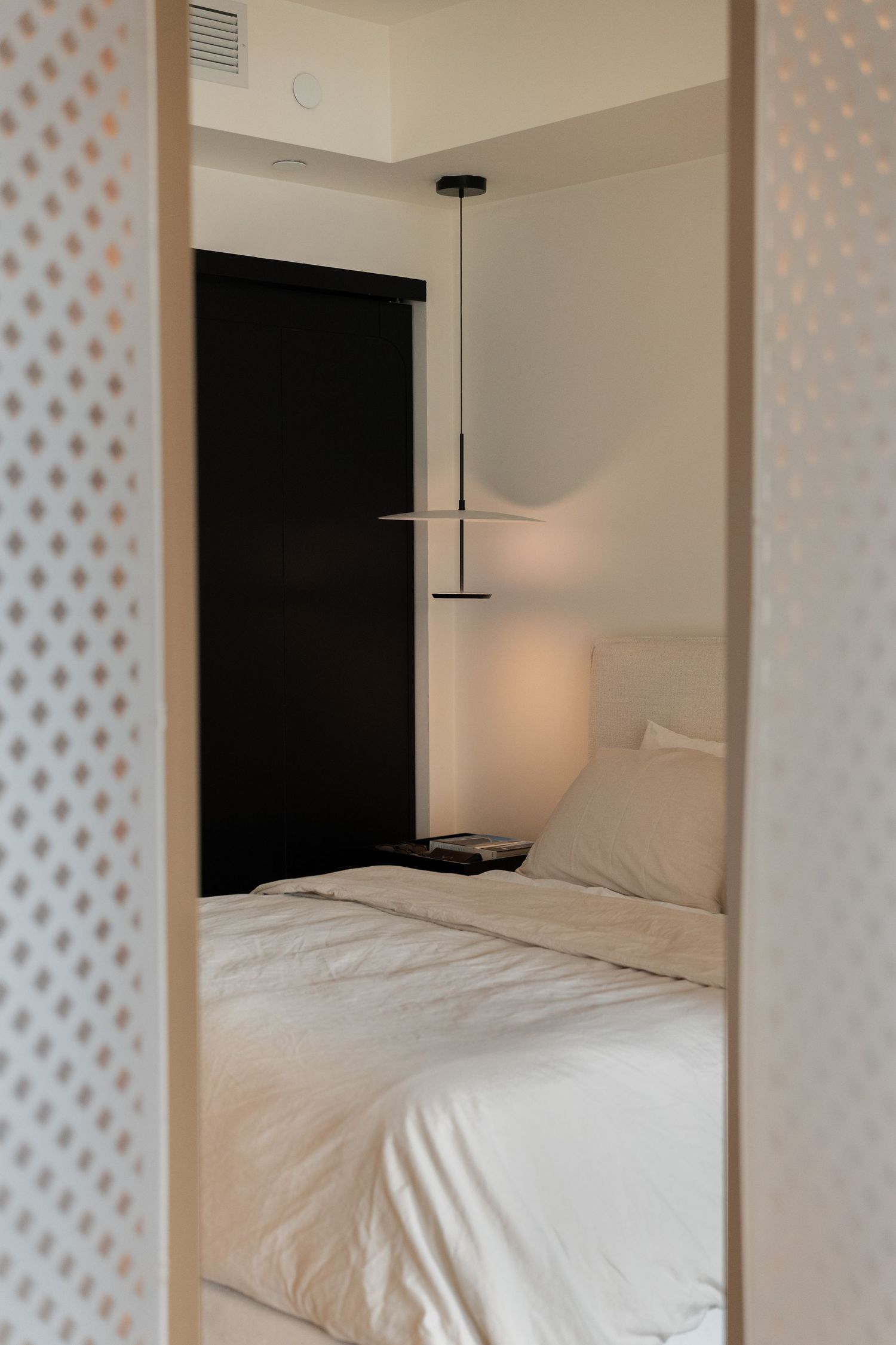 Cozy bedroom viewed through decorative lattice panel with pendant light and black sliding door.