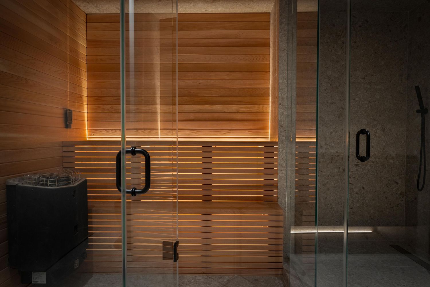 Luxury cedar wood sauna with glass door, bench lighting, and black sauna heater.