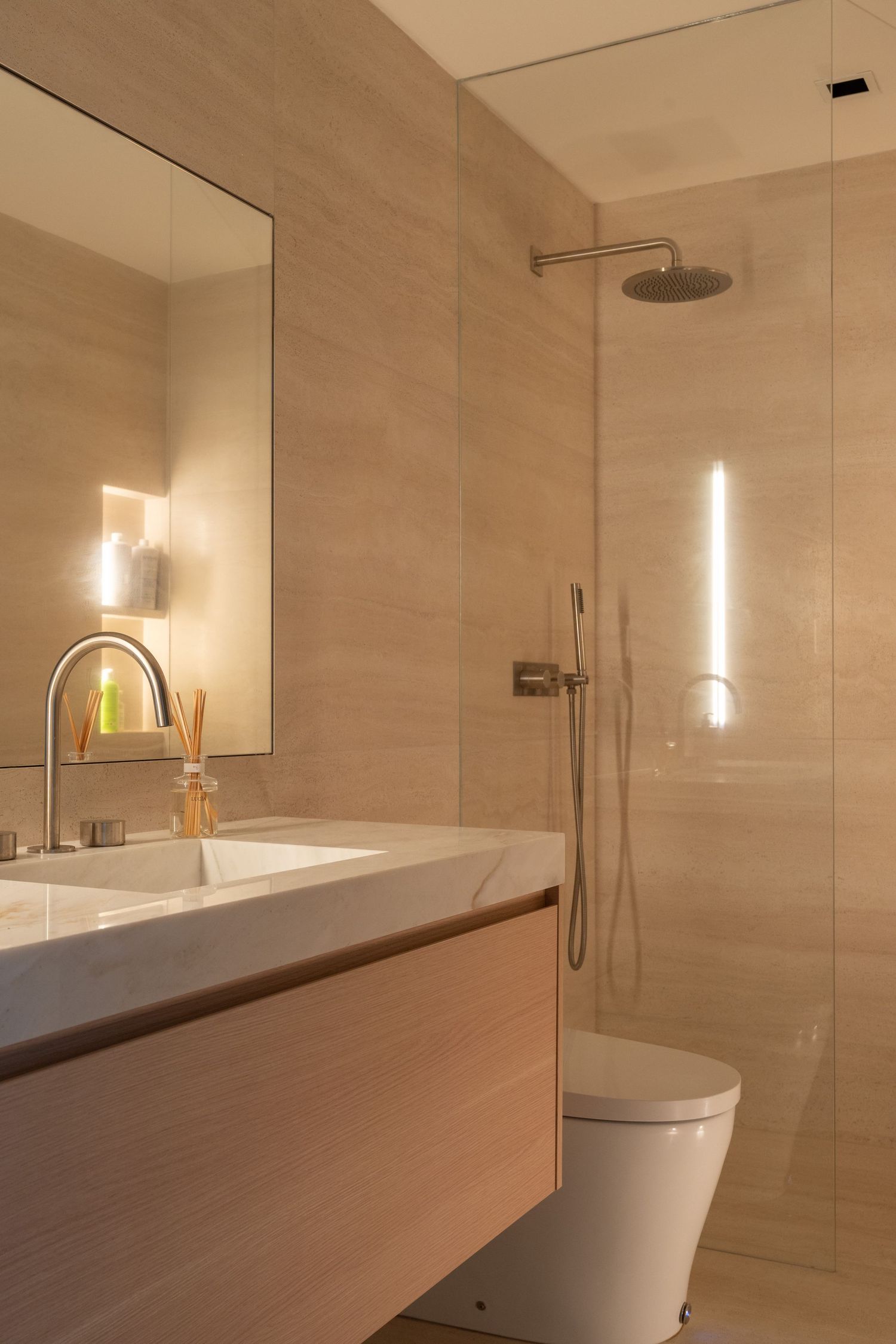 Modern beige bathroom with marble vanity, wall sconce, and glass shower enclosure.