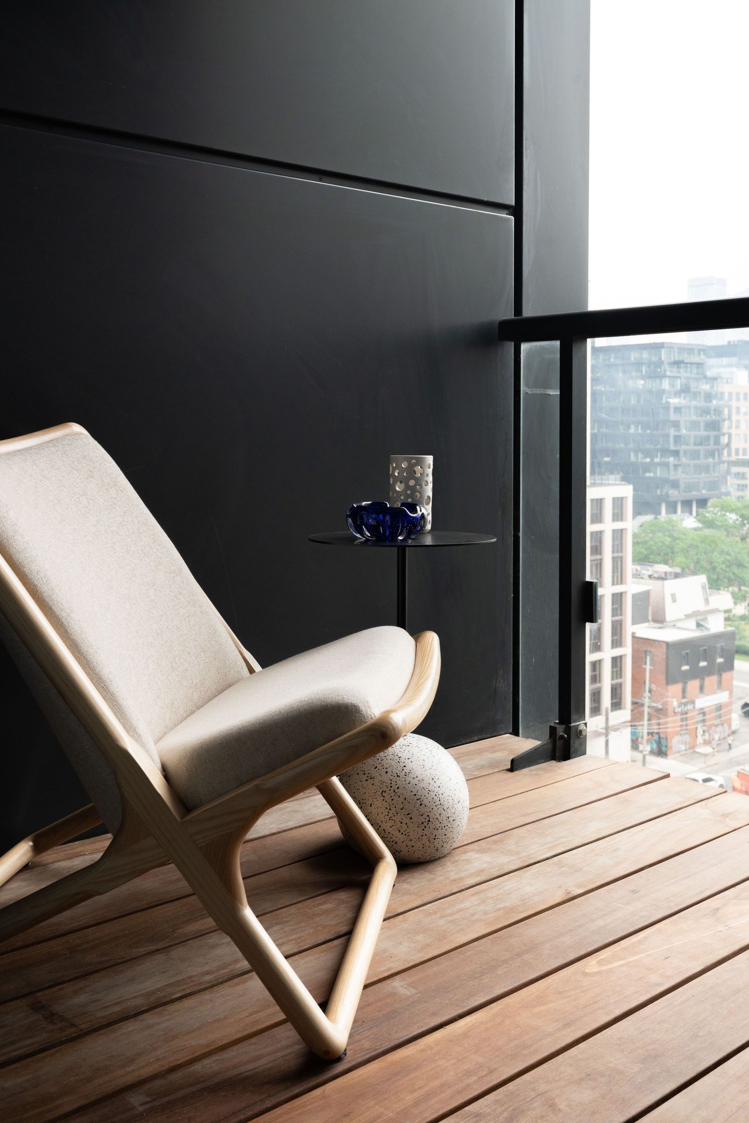Minimalist balcony with cream lounge chair, small side table, and city view.