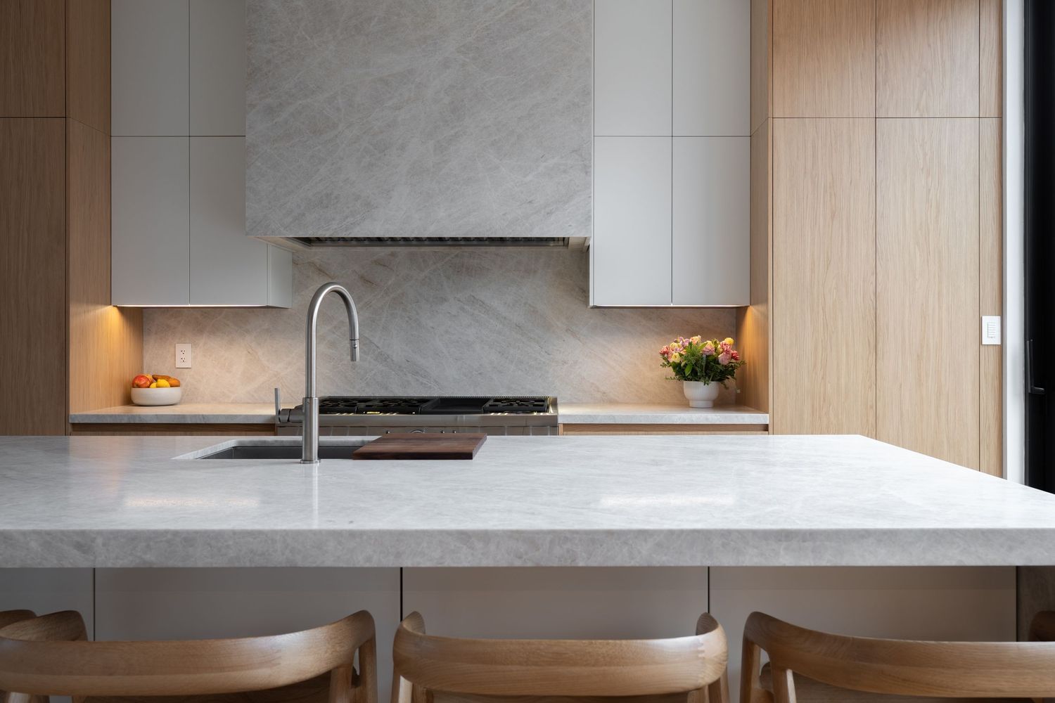 Elegant kitchen island with white marble countertop, integrated sink, wooden bar stools, and warm ambient lighting.