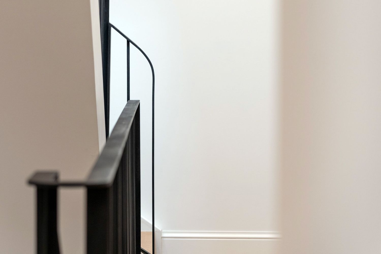 Minimalist interior detail showing a sleek black metal staircase railing against crisp white walls.