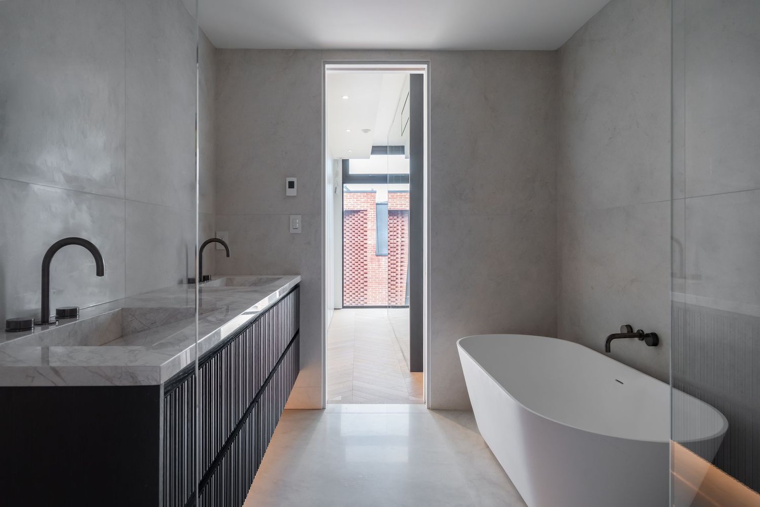 Minimalist bathroom with grey concrete walls, freestanding white soaking tub, dark vanity, and narrow skylight window.