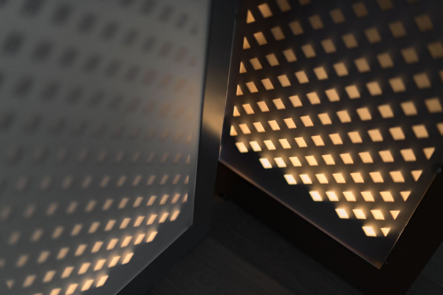 Close-up of decorative black metal perforated panel with warm backlit diamond pattern creating geometric shadow effects.