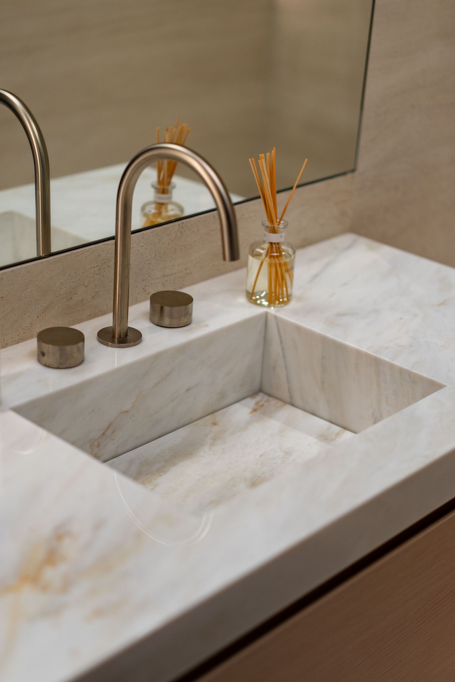 Luxury marble undermount bathroom sink with brushed gold widespread faucet and reed diffuser on stone vanity countertop.