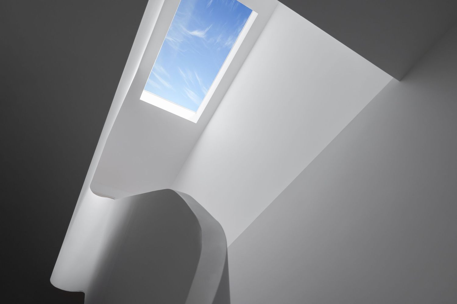Dramatic white sculptural staircase with curved walls and square skylight revealing blue sky above.